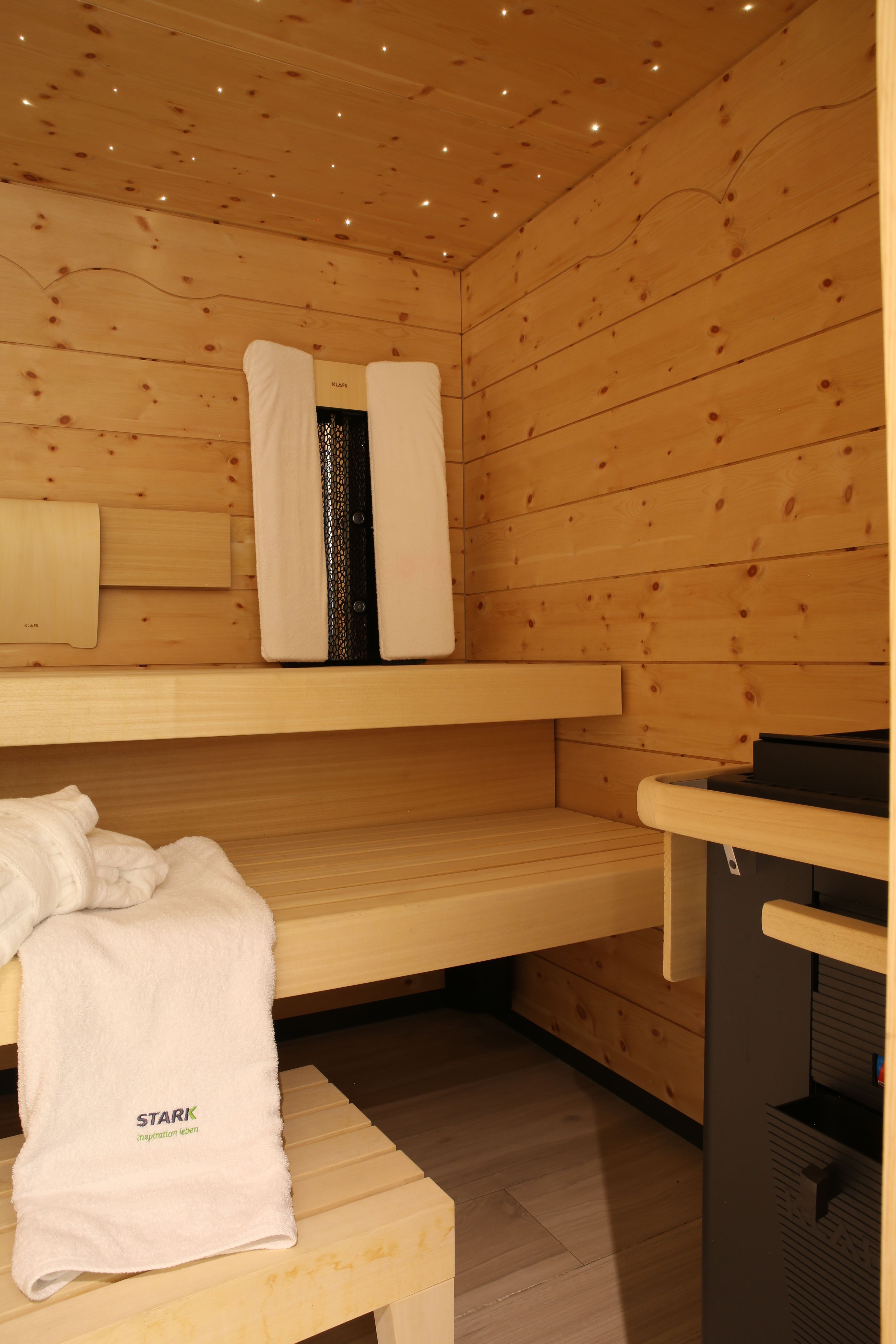 Sauna Grünwald — Saunaofen neben den Bänken, Handtuch mit Stark-Logo