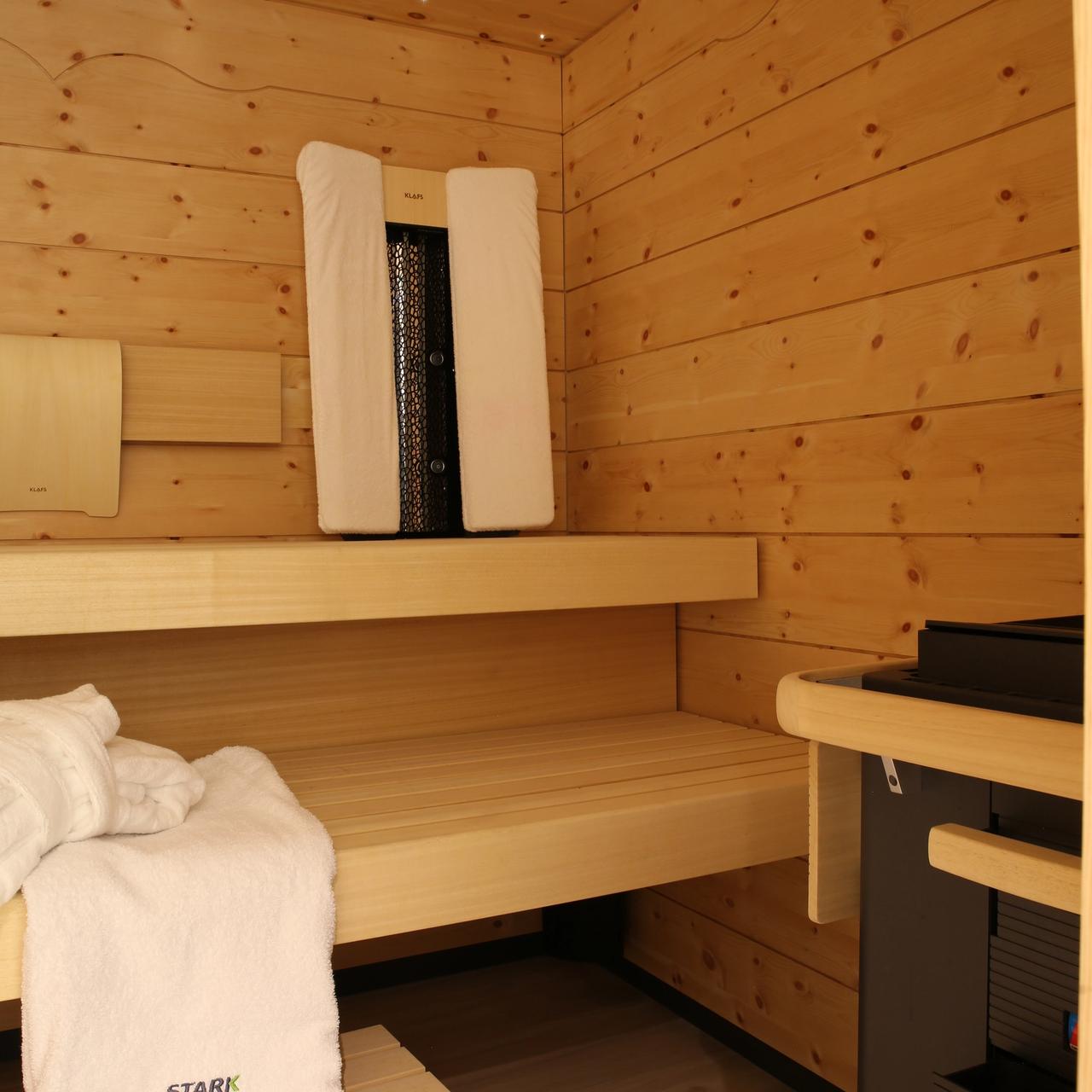 Sauna Grünwald — Saunaofen neben den Bänken, Handtuch mit Stark-Logo