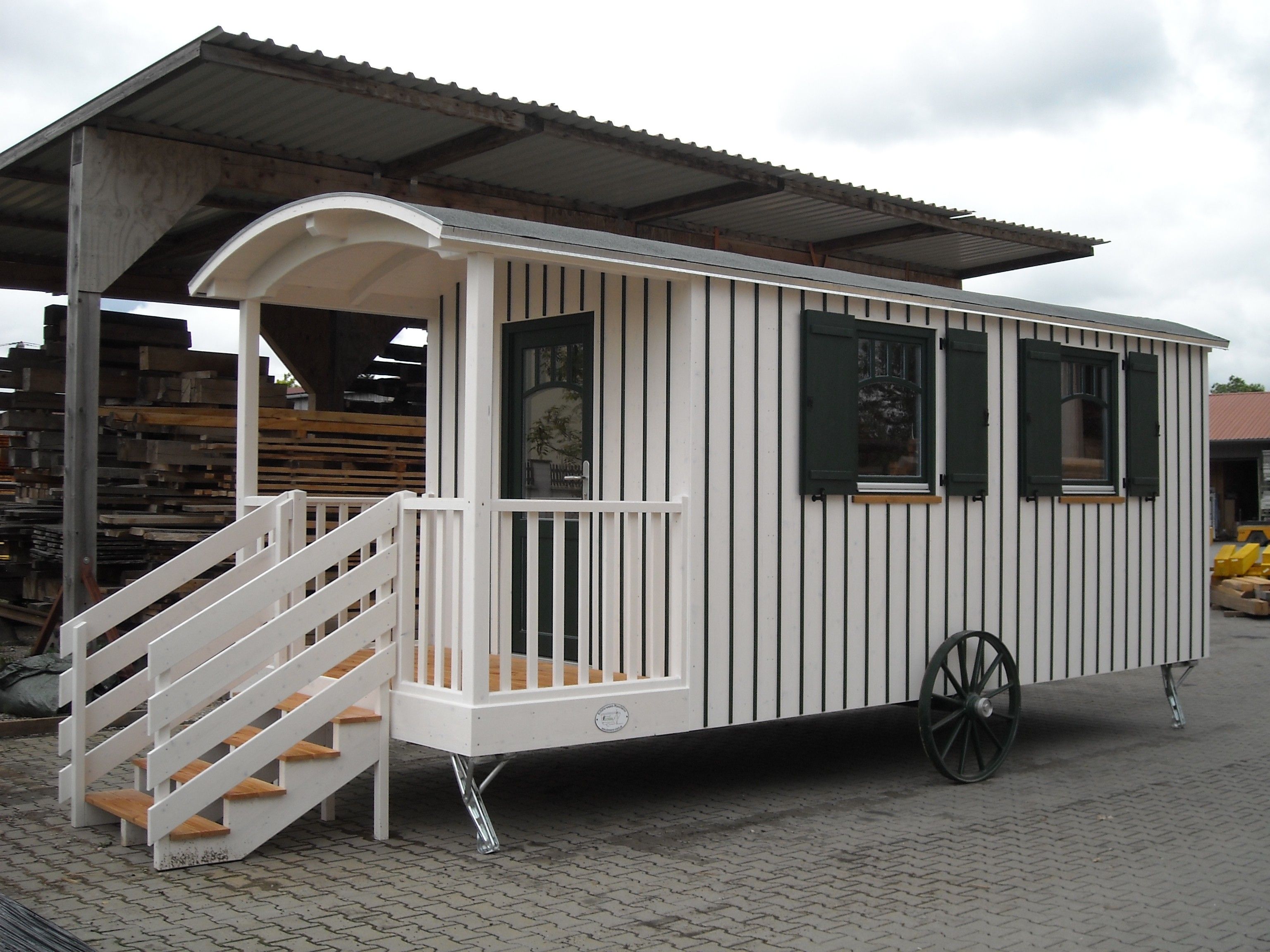 Weißer Zirkuswagen mit grünen Fensterläden, Speichenrad und überdachter Veranda mit Treppe