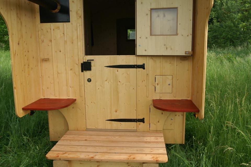 Eingang eines Schäferwagens mit Holztür, Trittstufe und zwei roten Klappsitzen