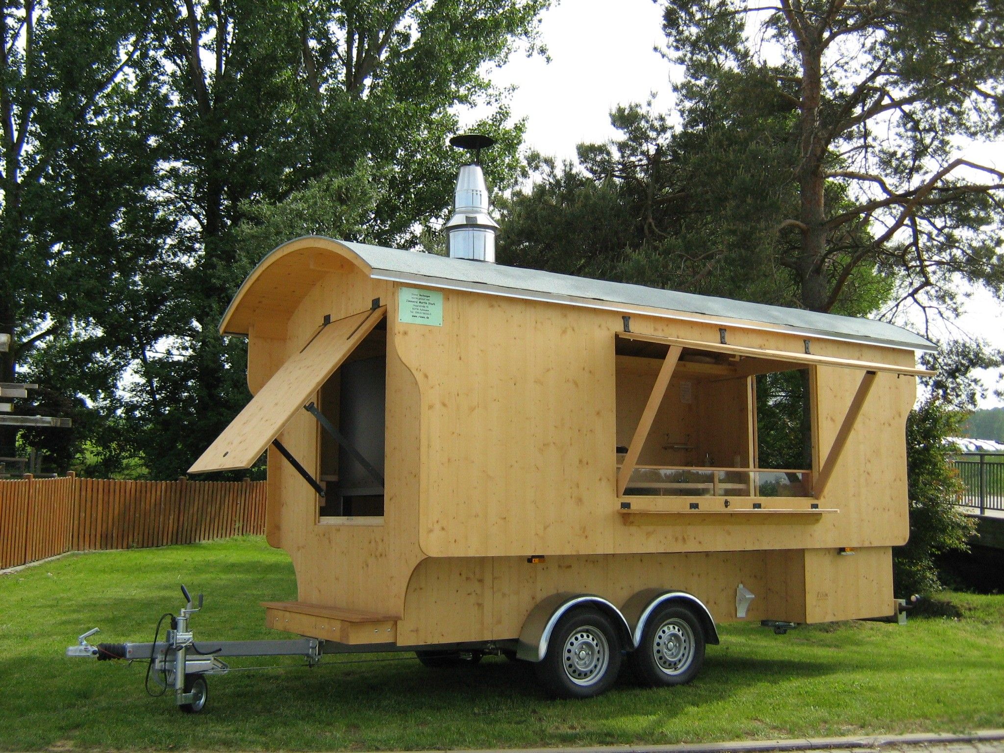 Backwagen aus hellem Holz mit hochgeklappten Verkaufsklappen auf einem Anhänger mit zwei Achsen