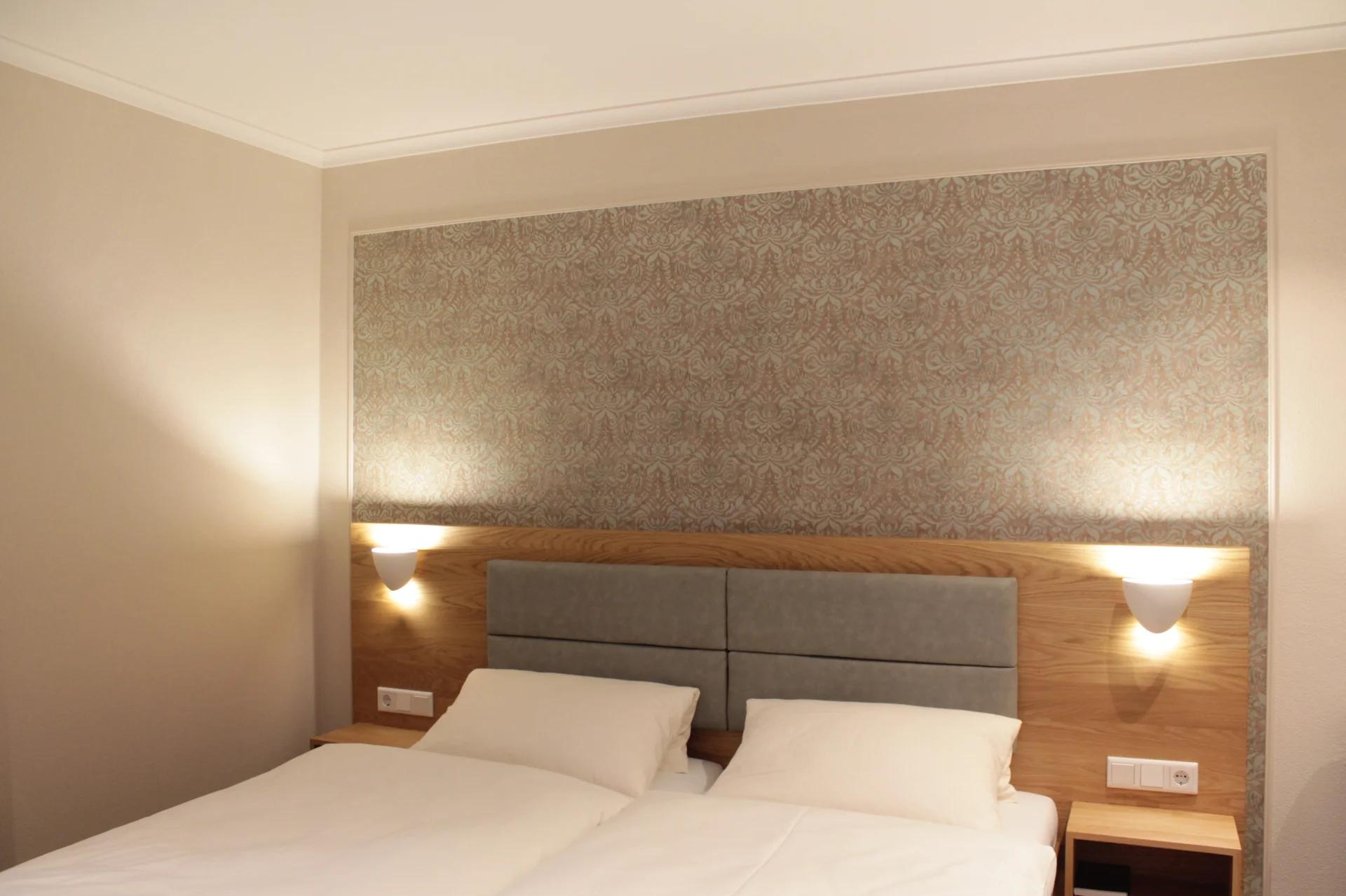 Hotelzimmer mit hölzernem Kopfteil und Wandleuchten auf beiden Seiten