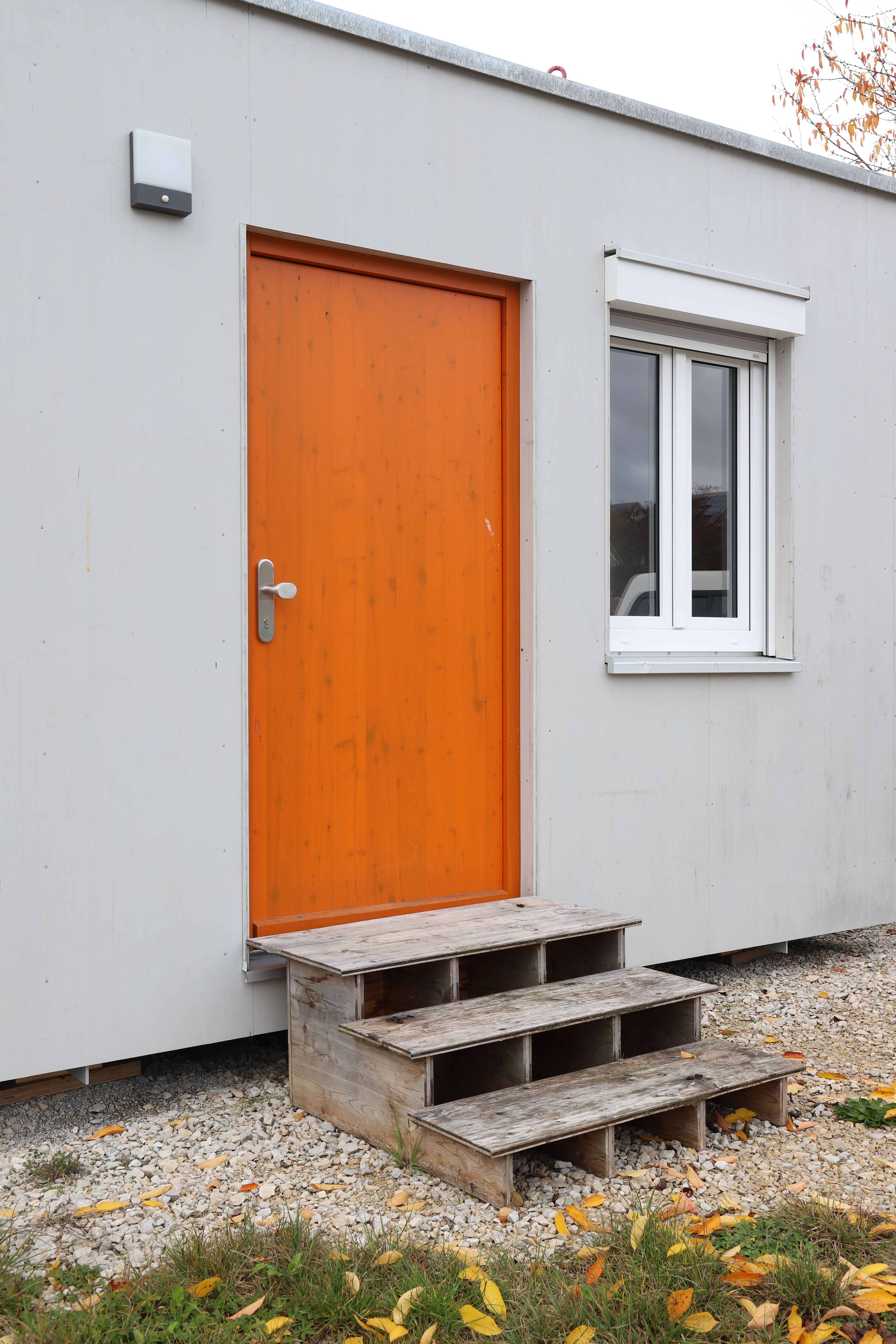 Orangefarbene Eingangstür und Holzregal an der hellen Fassade des TinyHouse