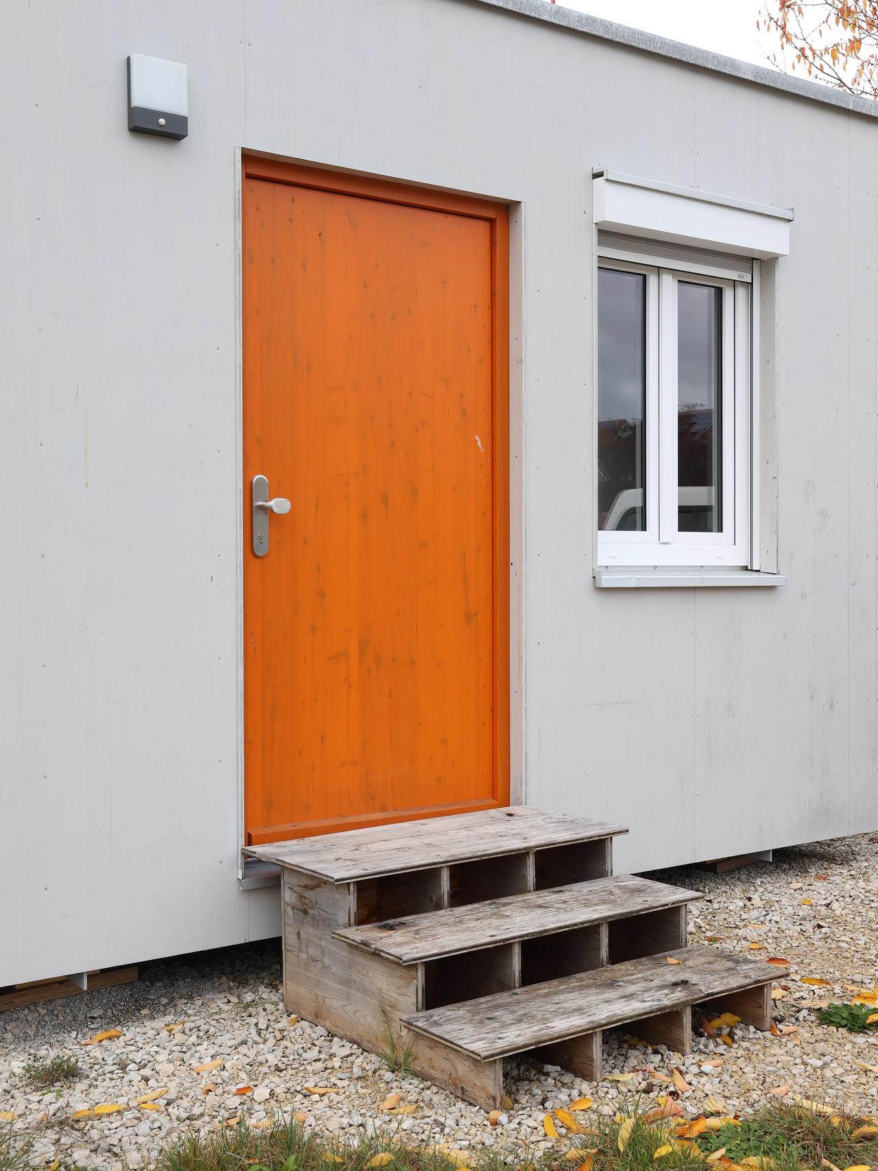 Orangefarbene Eingangstür und Holzregal an der hellen Fassade des TinyHouse