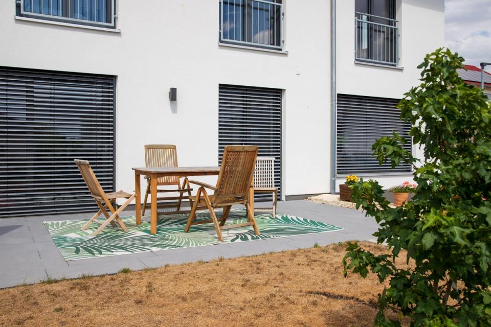Terrasse mit Holzmöbeln, Teppich und Raffstores an der Fassade