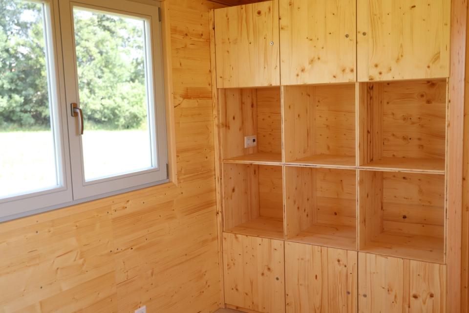Regalwand mit offenen Fächern und Schränken neben einem großen Fenster im Waldkindergartenwagen