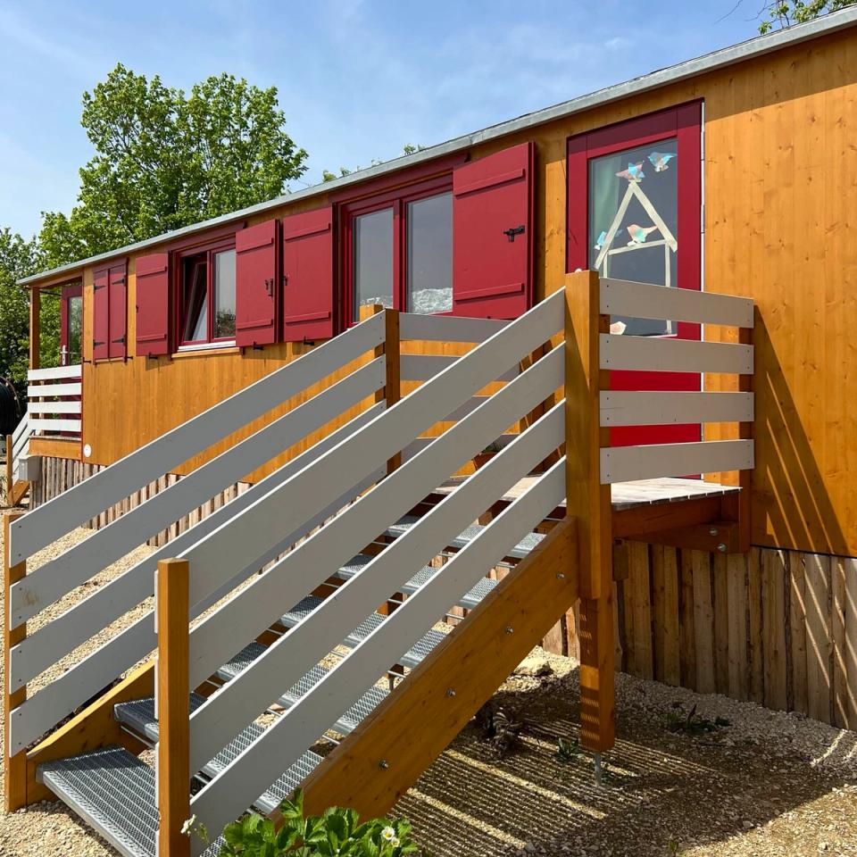 Treppe mit grauem Geländer zur roten Eingangstür eines Waldkindergartenwagens mit roten Fensterläden