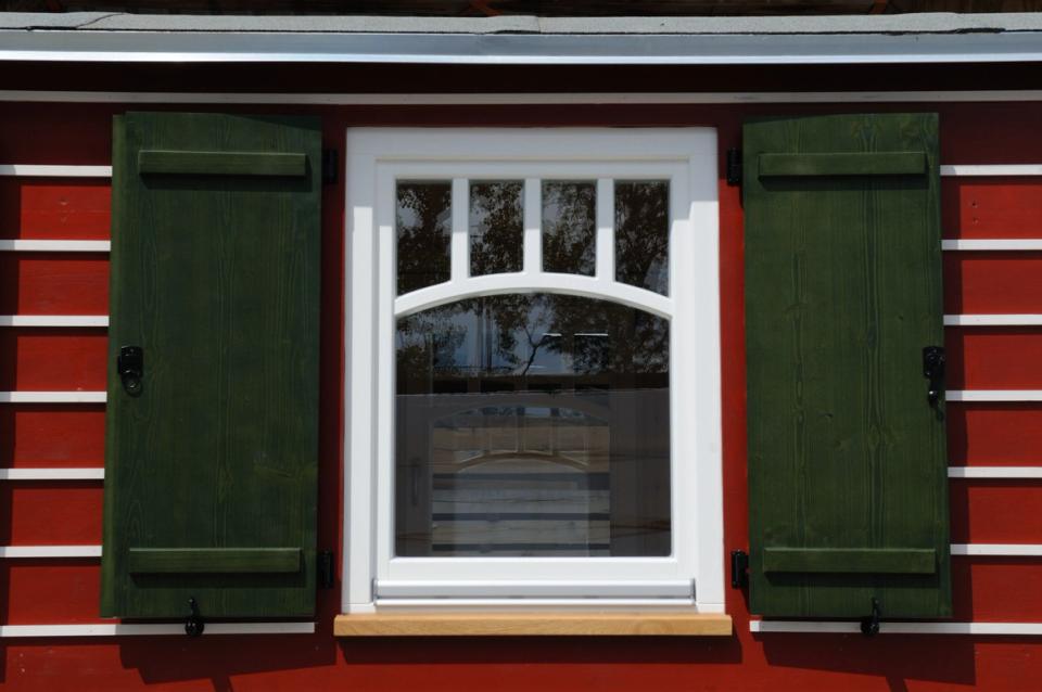 Sprossenfenster mit grünen Fensterläden an einem rot-weiß gestreiften Zirkuswagen