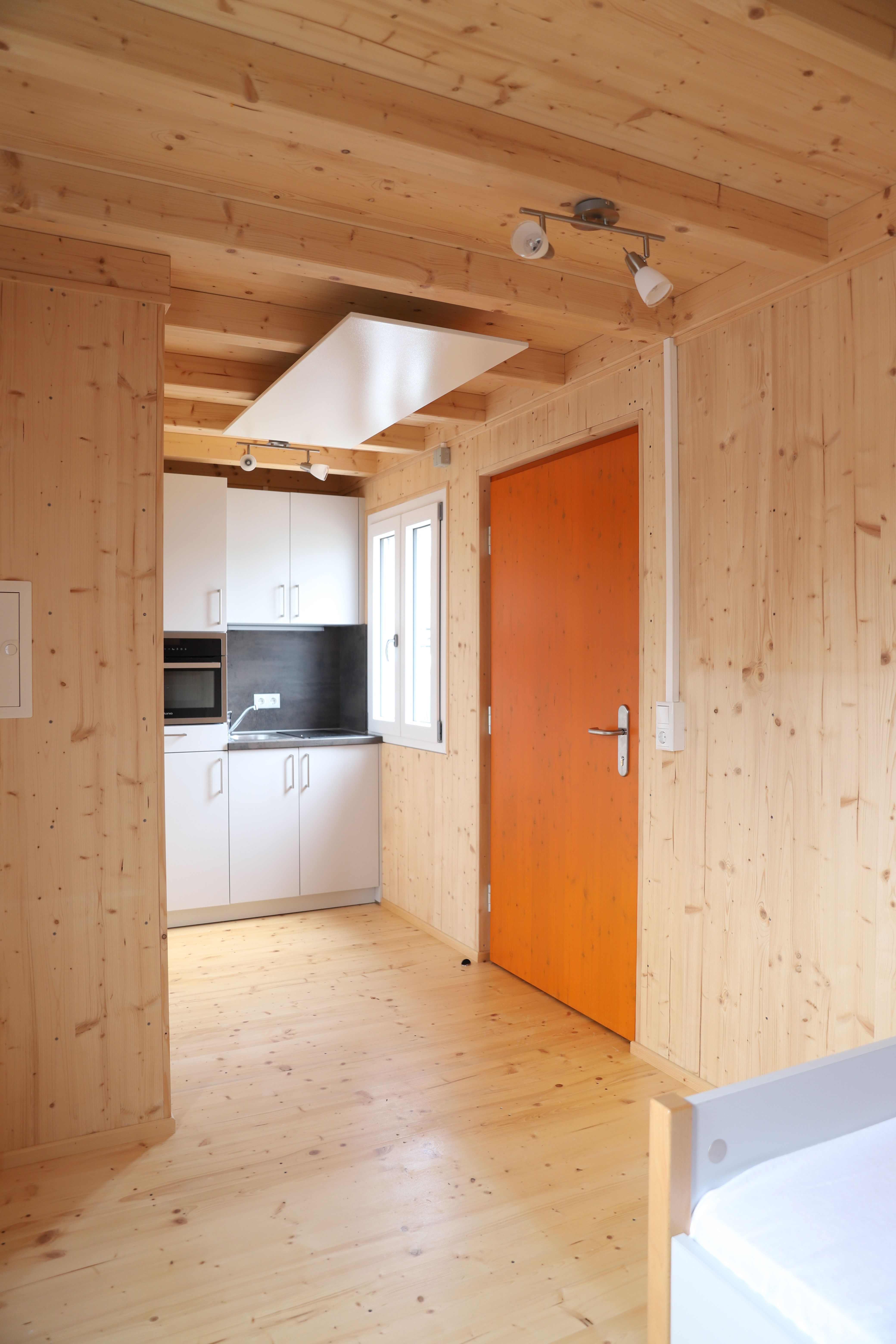 Wohnraum mit Küchenzeile und orangefarbener Tür im TinyHouse