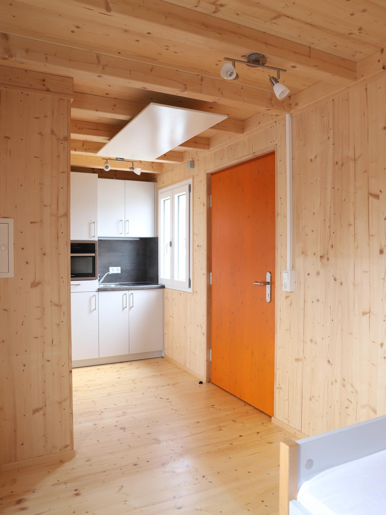 Wohnraum mit Küchenzeile und orangefarbener Tür im TinyHouse