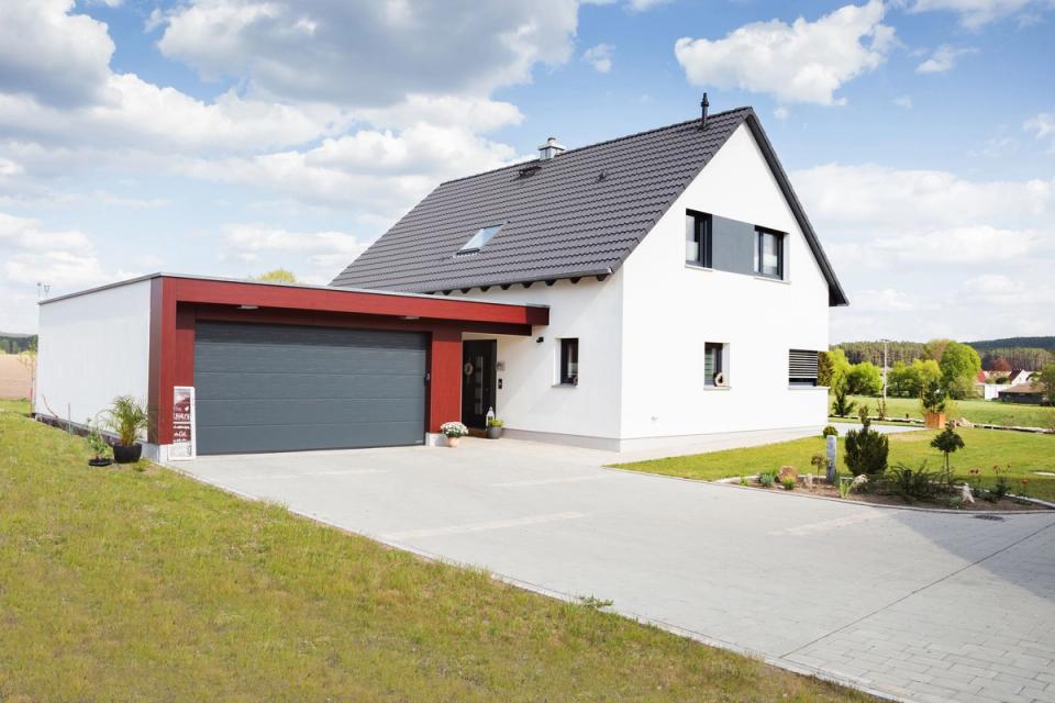 Weißes Satteldachhaus mit roter Garage und Vorgarten in Feldlage