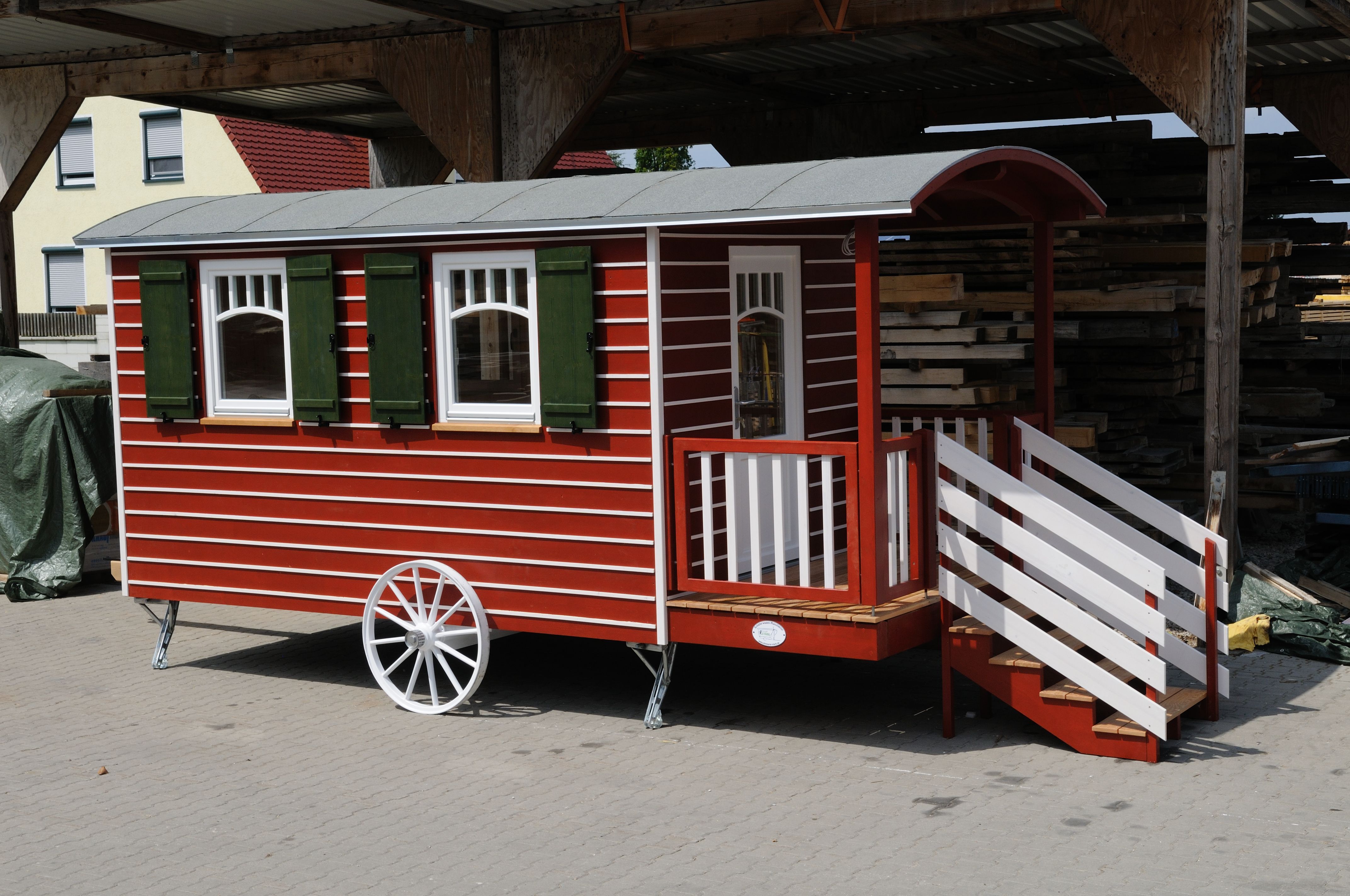 Roter Zirkuswagen mit grünen Fensterläden, Veranda und weißem Speichenrad