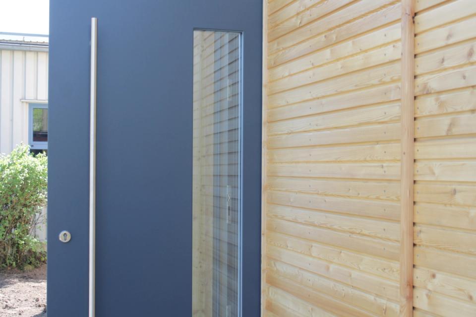 Anthrazitfarbene Eingangstür mit Glasausschnitt in der Lärchenfassade