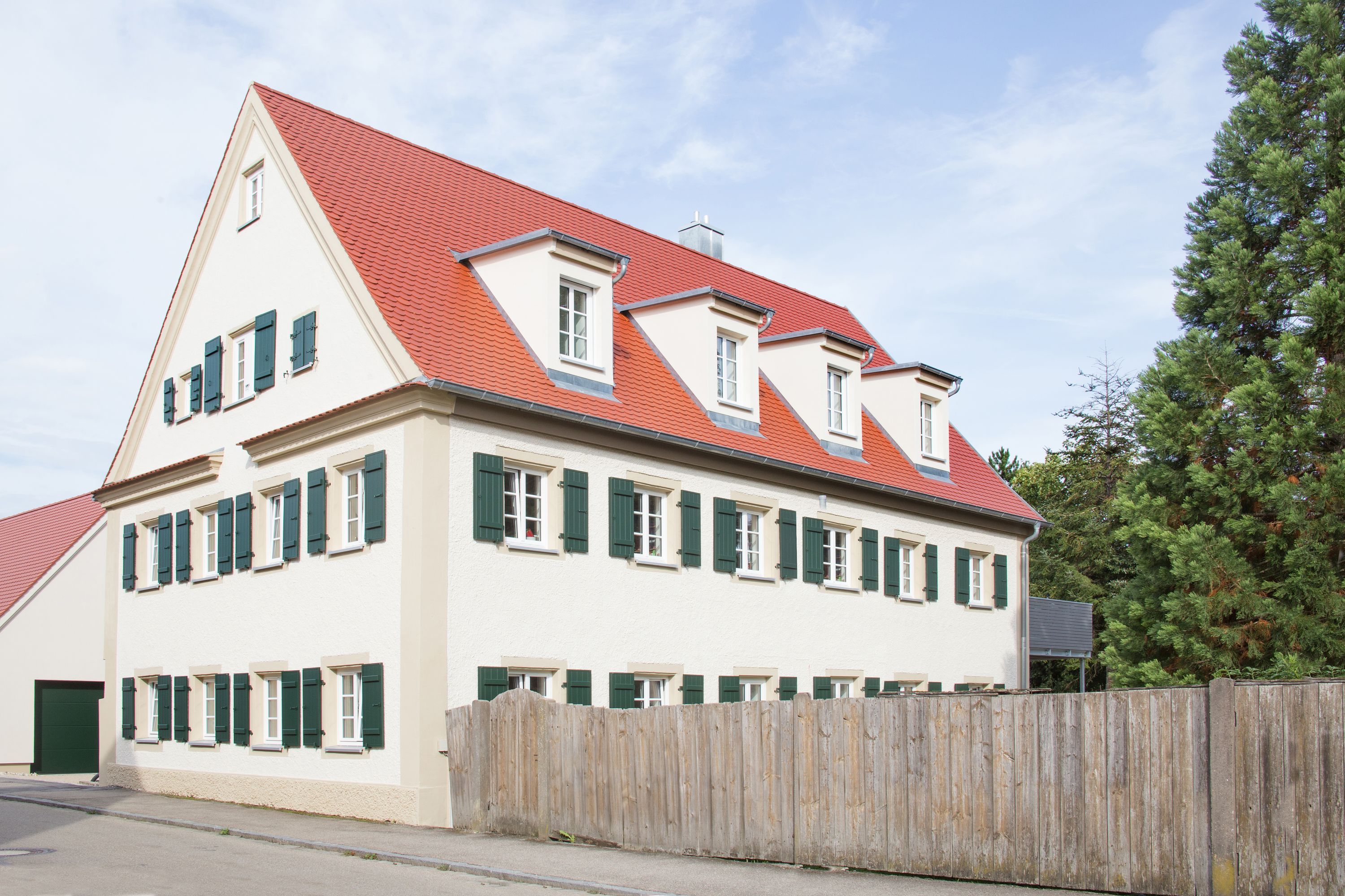 Saniertes Wohnhaus mit rotem Ziegeldach, grünen Fensterläden und Gauben
