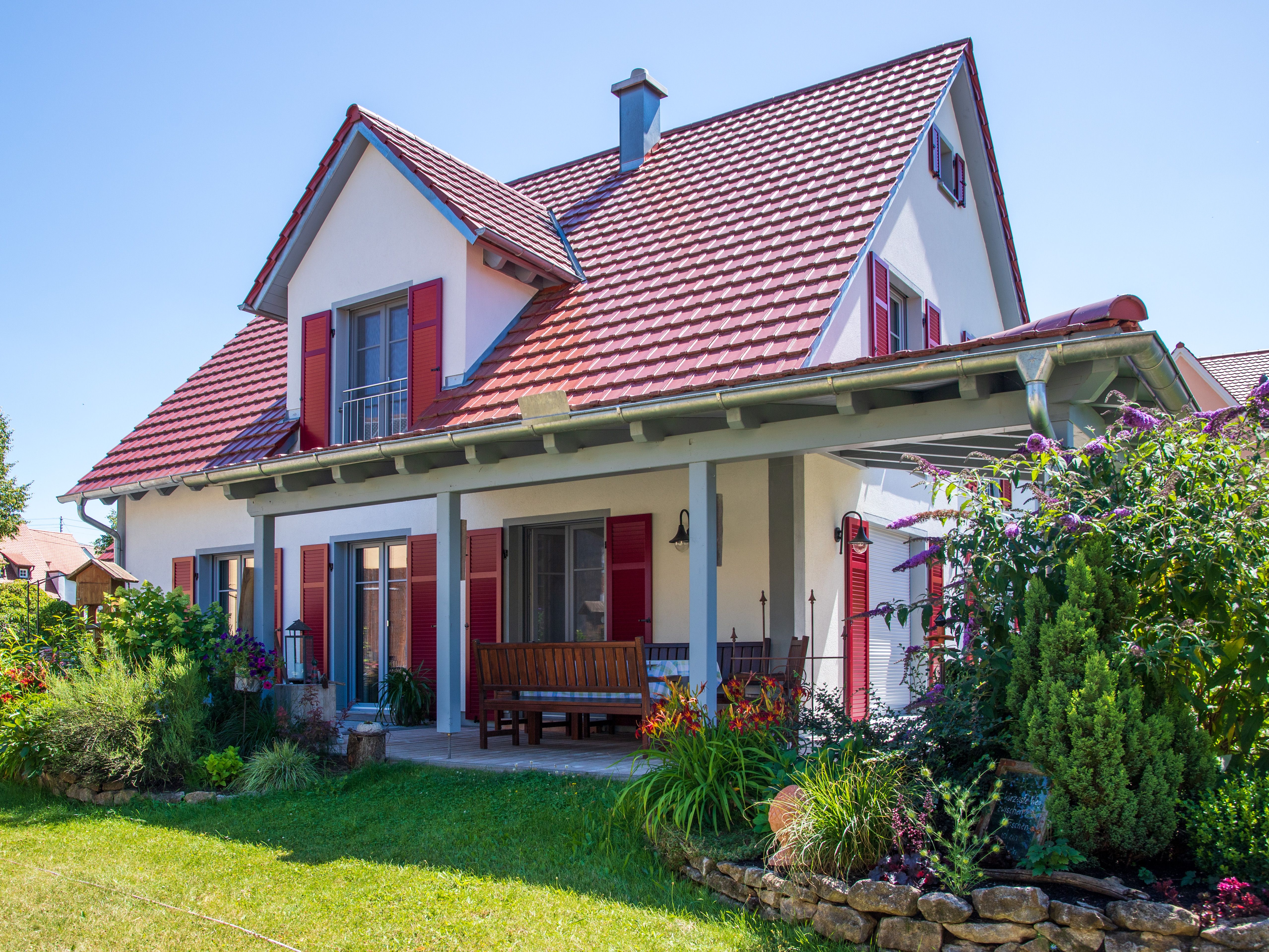Landhaus mit rotem Dach, roten Fensterläden und blühendem Garten