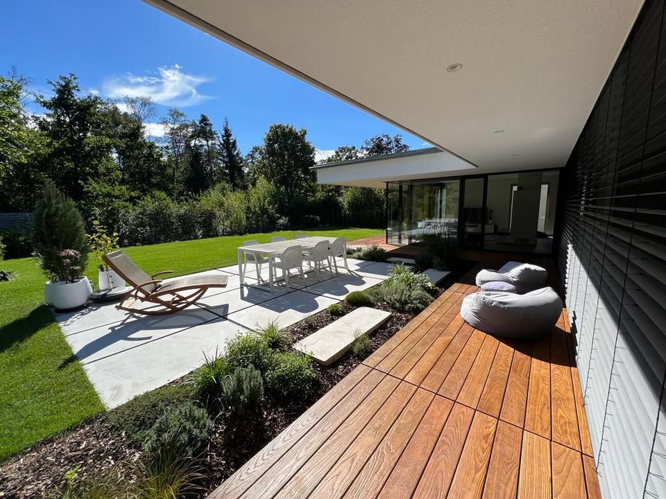 Überdachte Holzterrasse mit Sitzmöbeln und gepflasterter Gartenterrasse