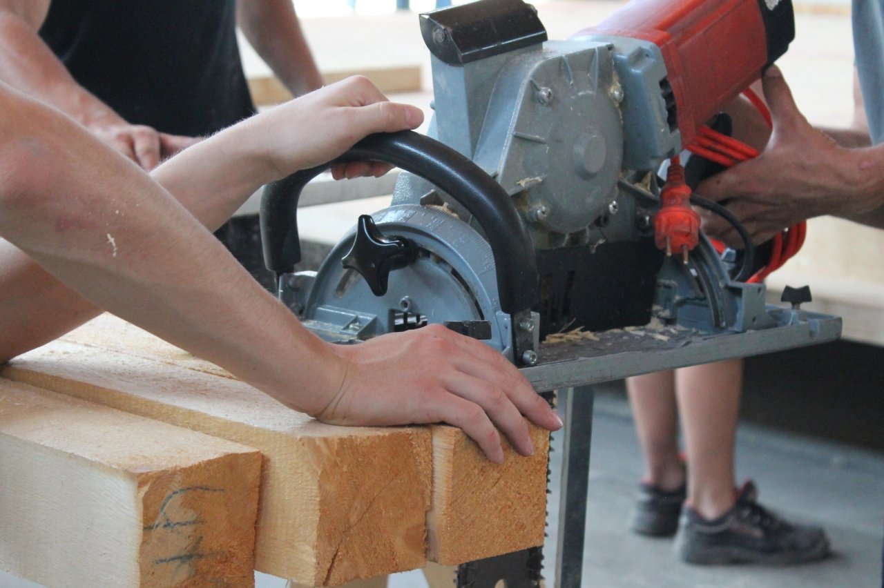 Besucher führen an einem Stand der Zimmerei Stark eine Handkreissäge durch einen Holzbalken