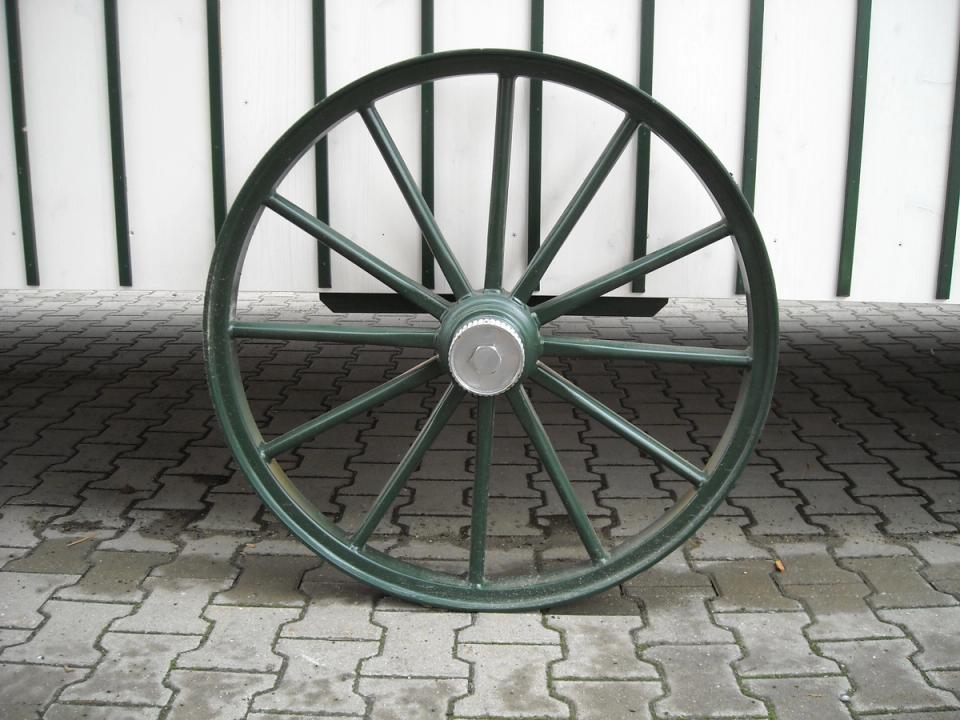 Grünes Speichenrad mit Eisenreifen unter einem Zirkuswagen