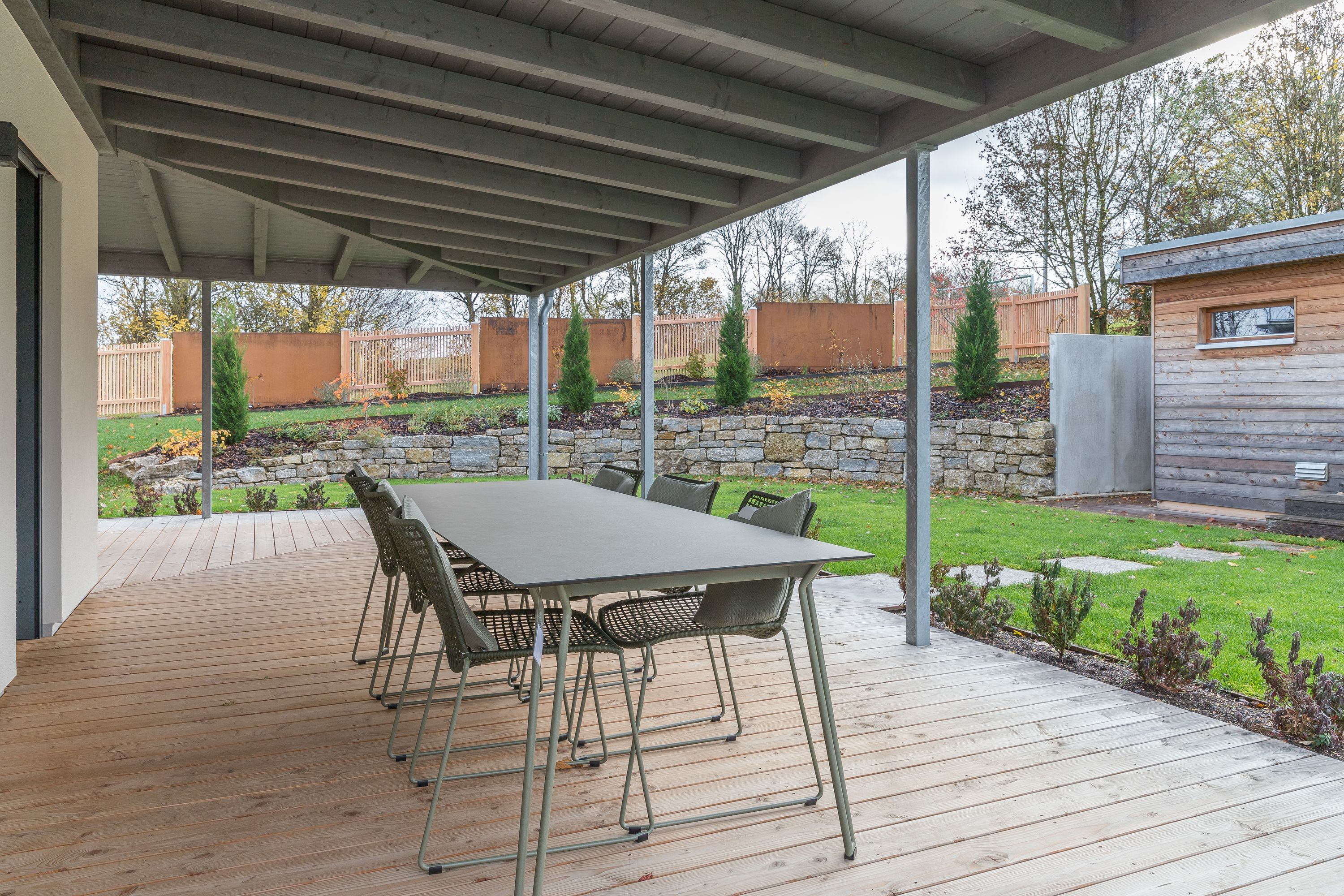 Überdachte Holzterrasse mit Esstisch und Blick in den herbstlichen Garten