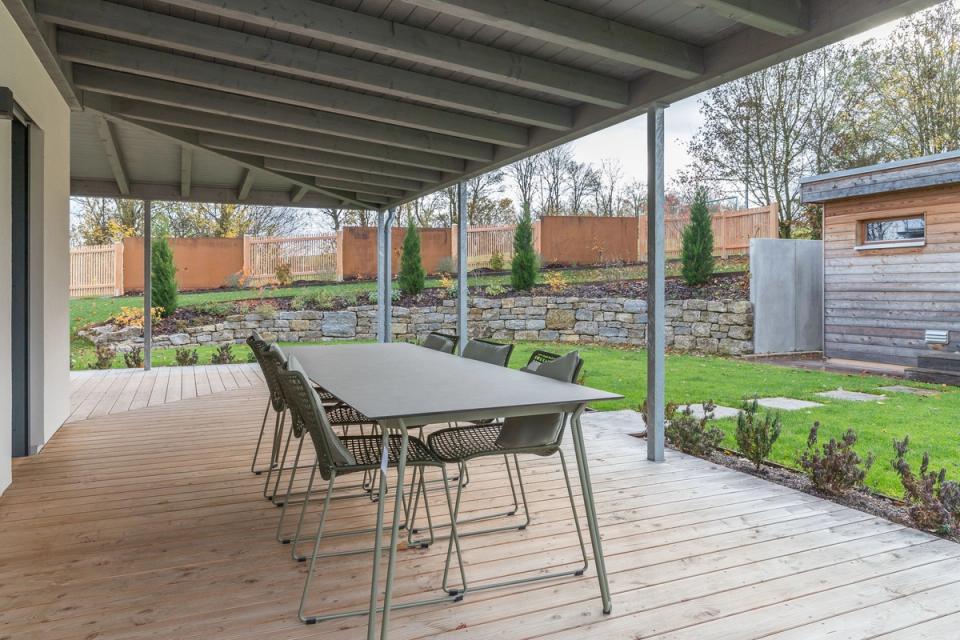 Überdachte Holzterrasse mit Esstisch und Blick auf herbstlichen Garten