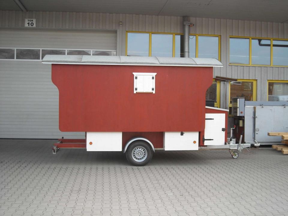 Roter Schäferwagen auf einem Anhänger von der Seite vor einer Werkhalle