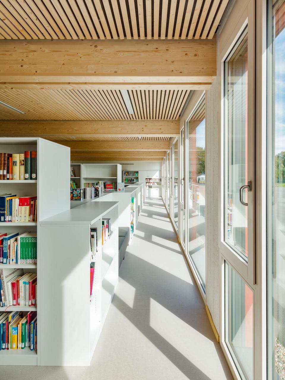 Schulbibliothek mit weißen Regalen entlang bodentiefer Fensterfront