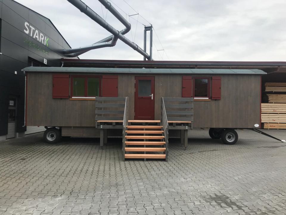 Graubrauner Waldkindergartenwagen von vorn mit roter Tür, Podest und breiter Holztreppe