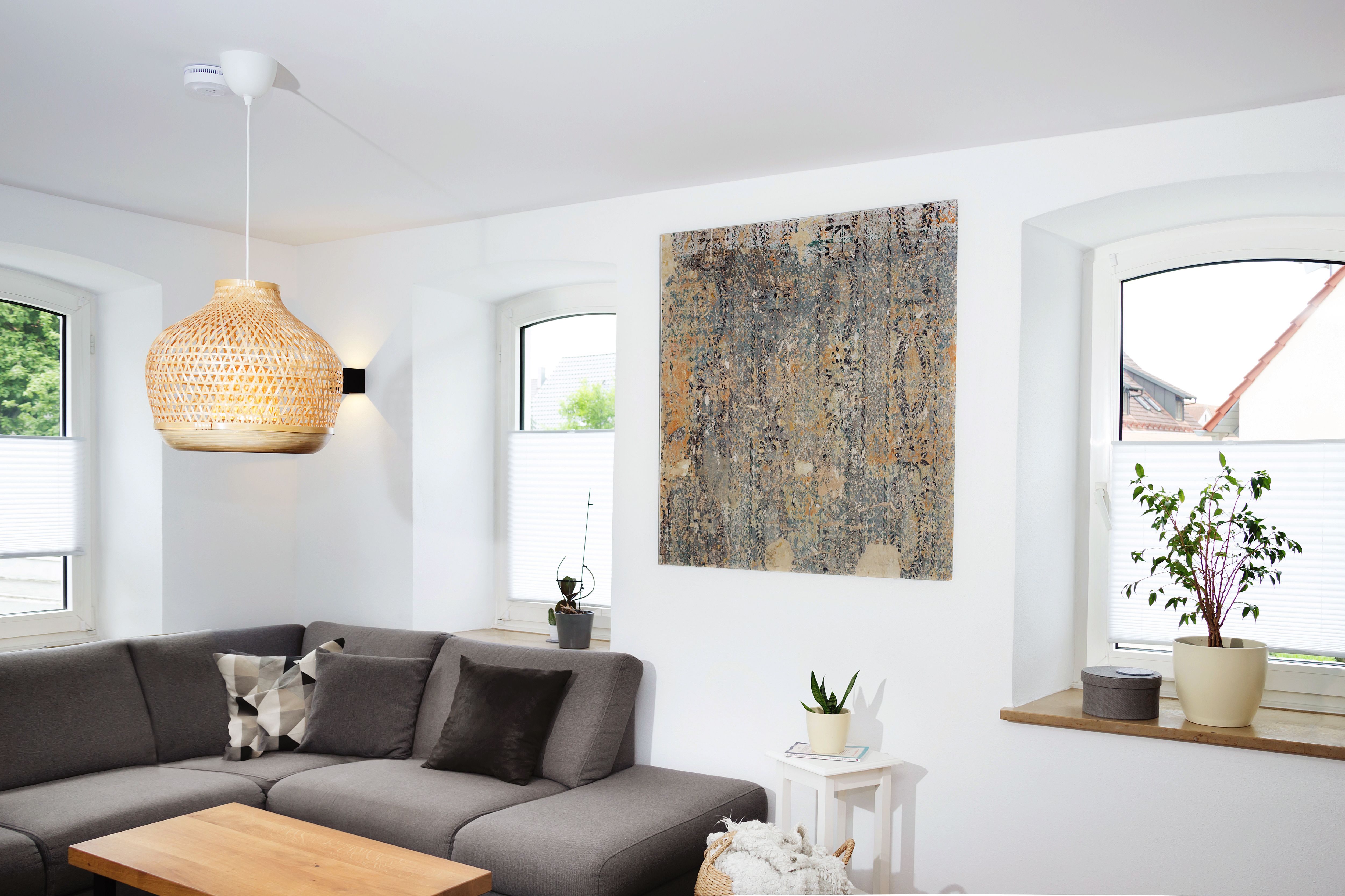 Wohnzimmerecke mit Sofa, Rattanleuchte und großem Wandbild