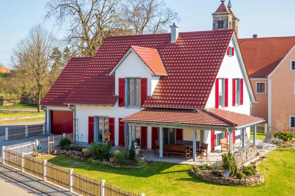Einfamilienhaus mit rotem Satteldach und roten Fensterläden im Dorf