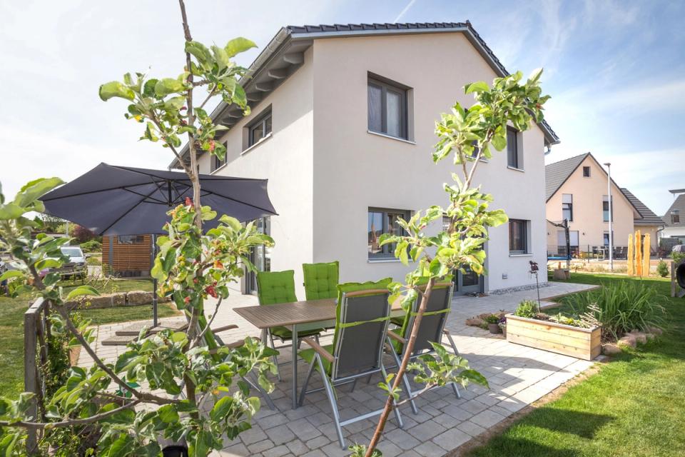 Sitzterrasse mit Gartenmöbeln und Sonnenschirm hinter dem Haus