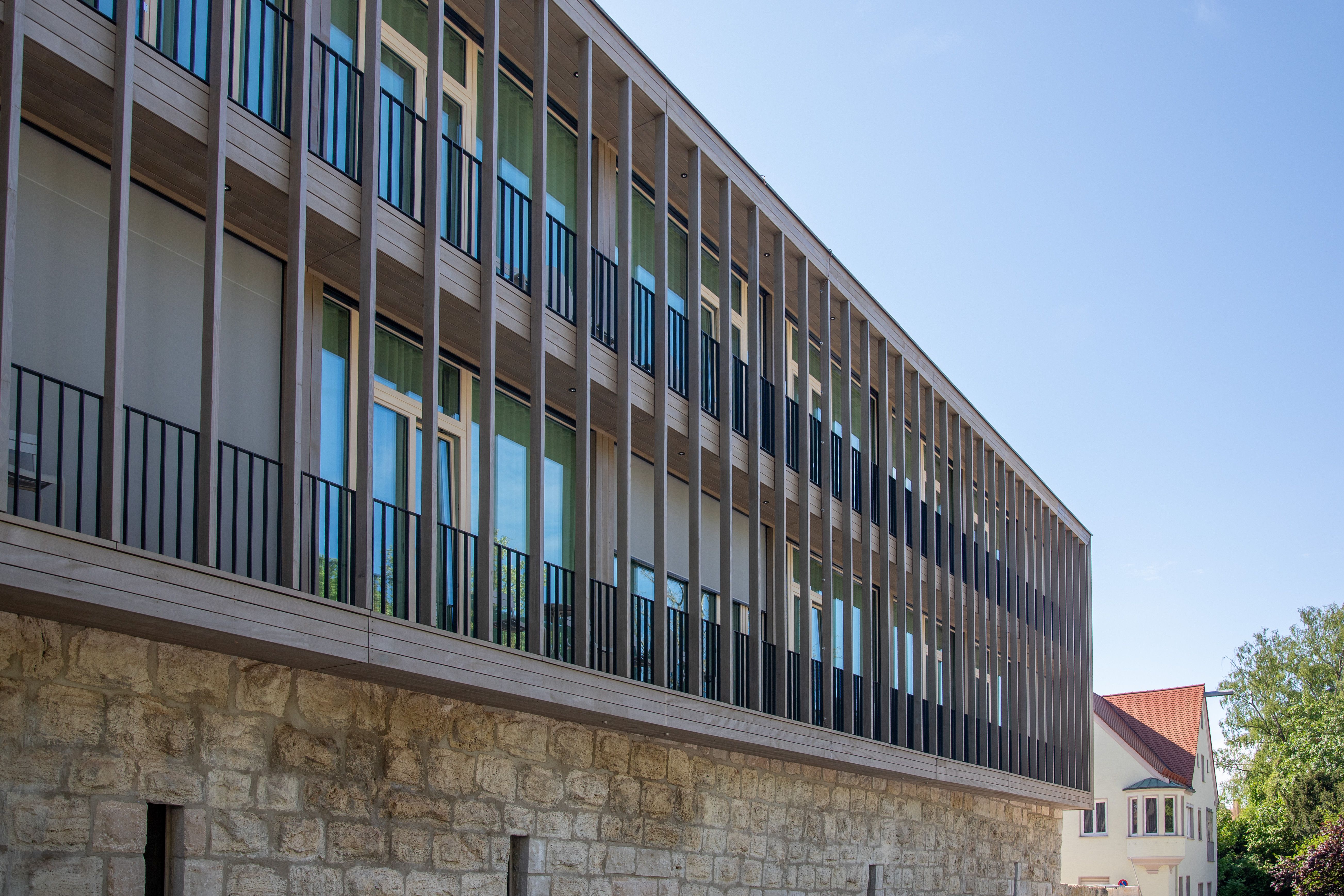 Holzlamellenfassade des Hotelneubaus über historischer Natursteinmauer