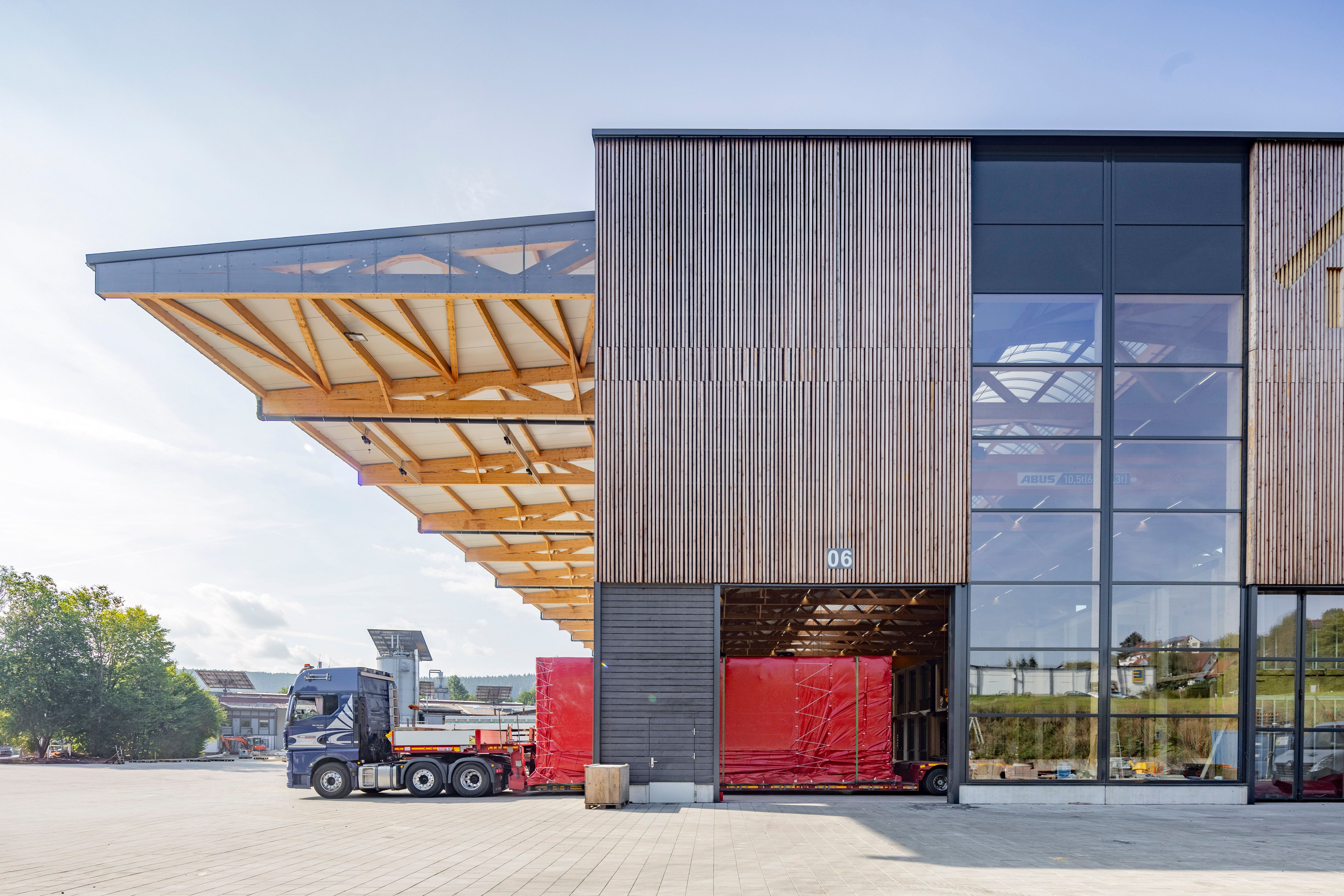 Produktionshalle der Zimmerei Stark mit Holzfassade — Sattelzug lädt ein Bauteil