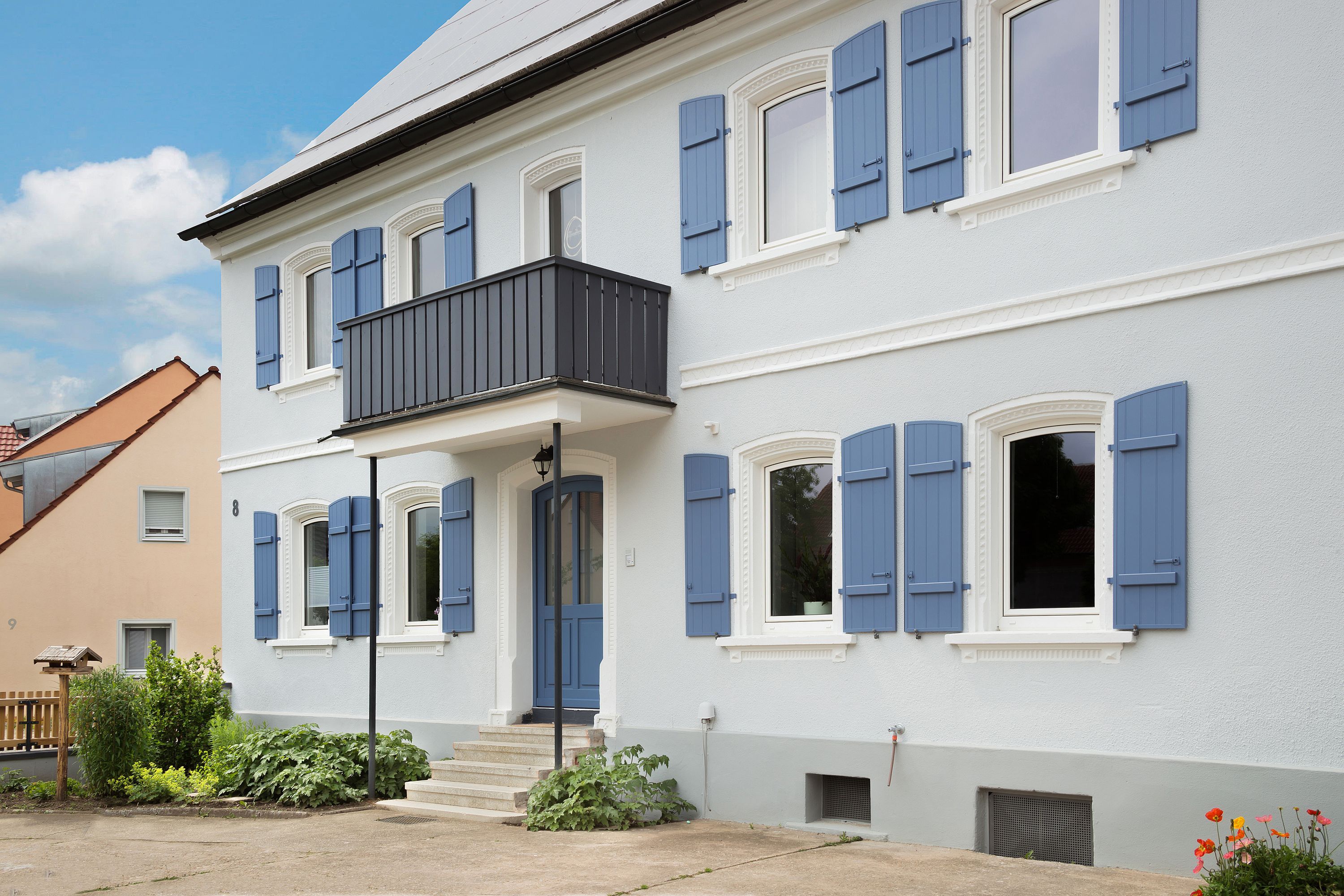 Sanierte Fassade über Eck mit Eingang, Balkon und blauen Läden