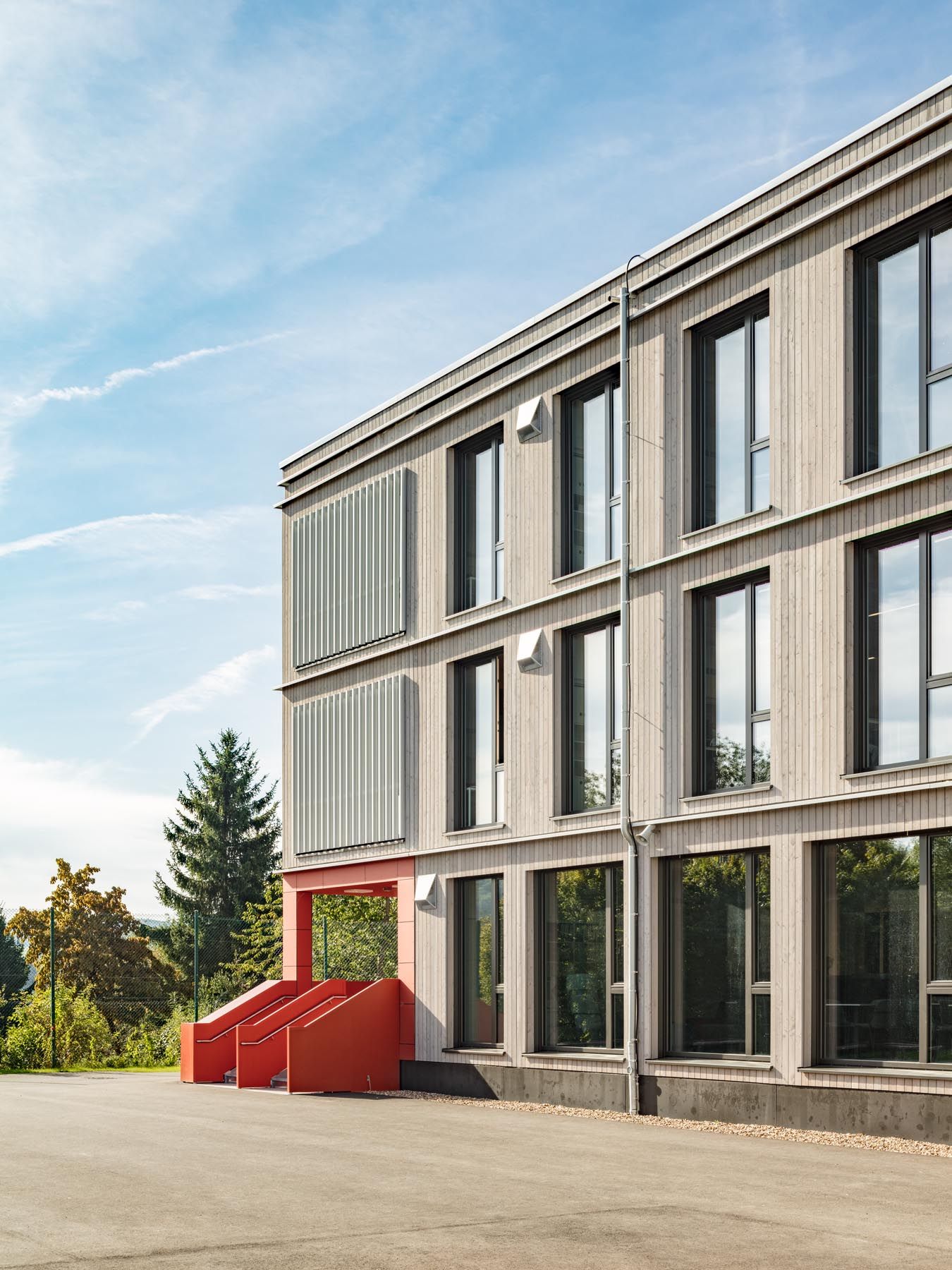 Vergraute Holzfassade der Interimsschule in Prüm mit rotem Eingangsbereich