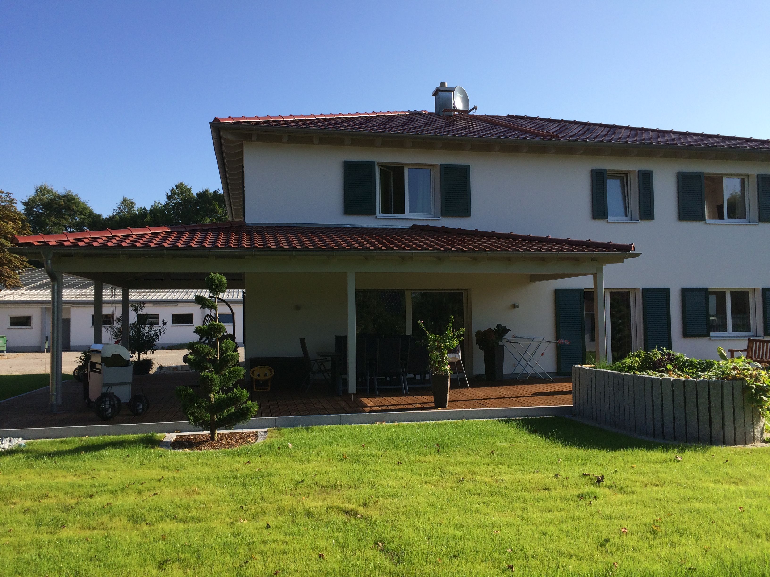 Weißes Einfamilienhaus mit Walmdach, überdachter Terrasse und Carport im Garten