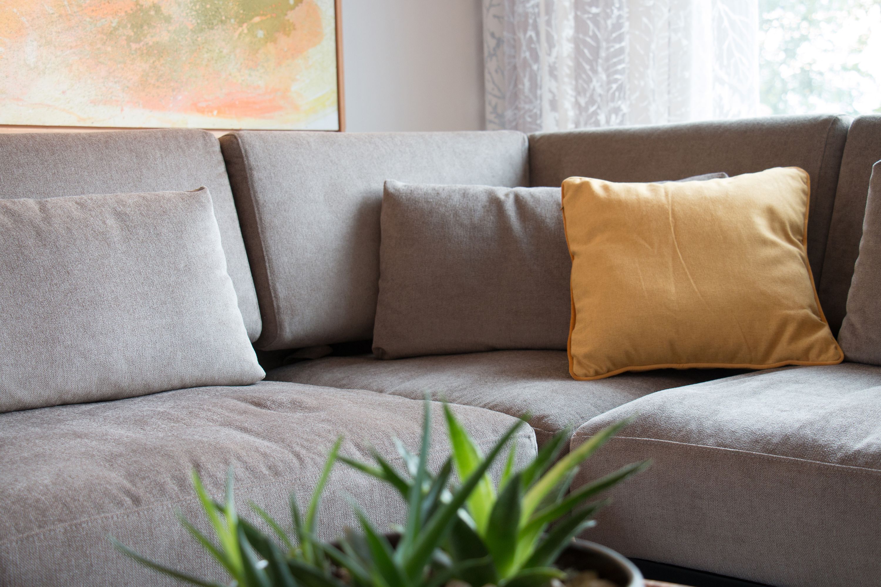Graues Sofa mit senfgelbem Kissen im Wohnzimmer des Musterhauses 2inEins