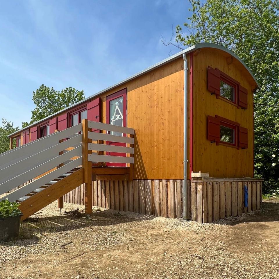 Rückseite eines honigfarbenen Waldkindergartenwagens mit gewölbtem Dach und roten Fensterläden