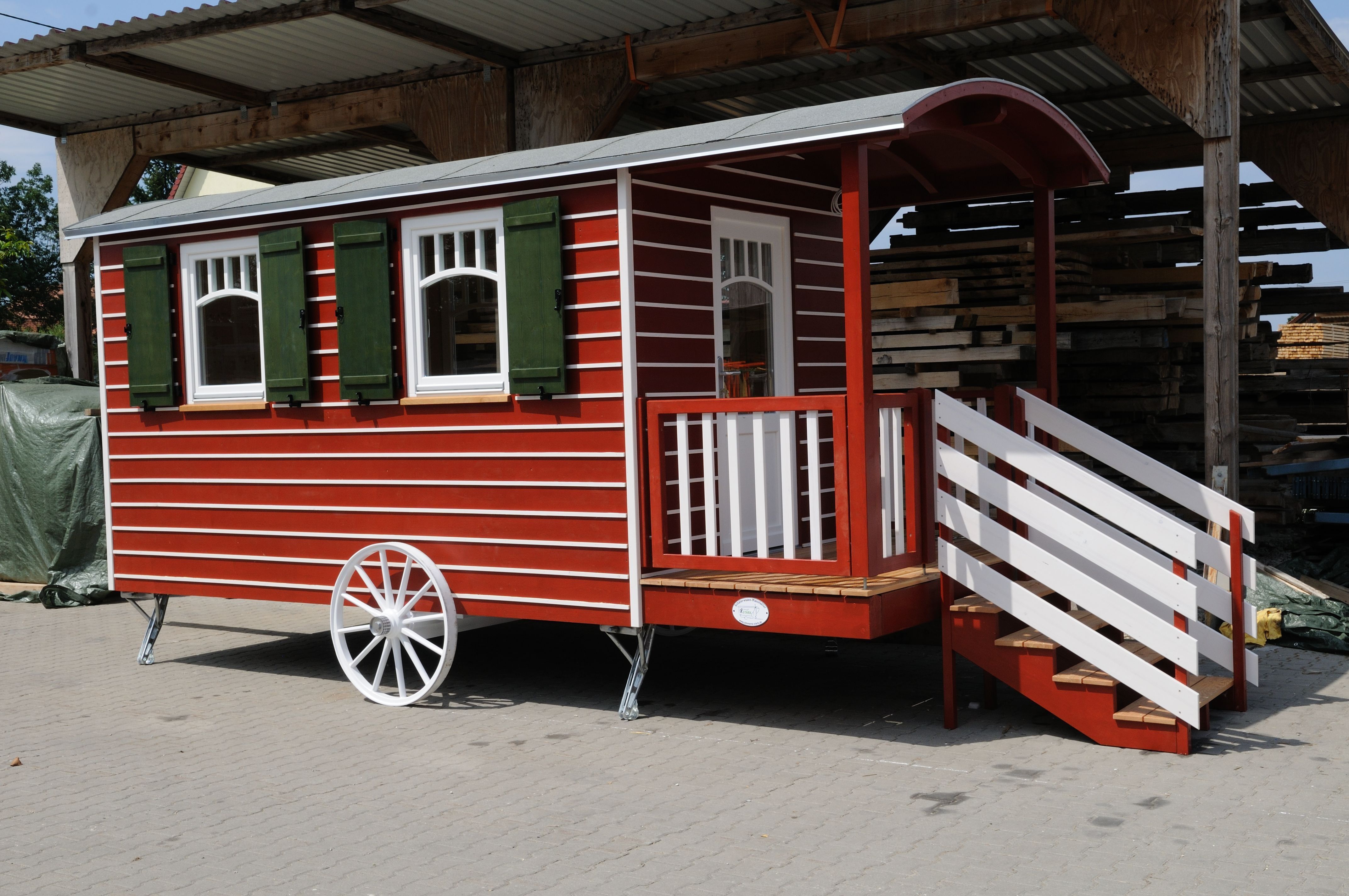 Rot-weiß gestreifter Zirkuswagen mit grünen Fensterläden, weißen Speichenrädern und Veranda