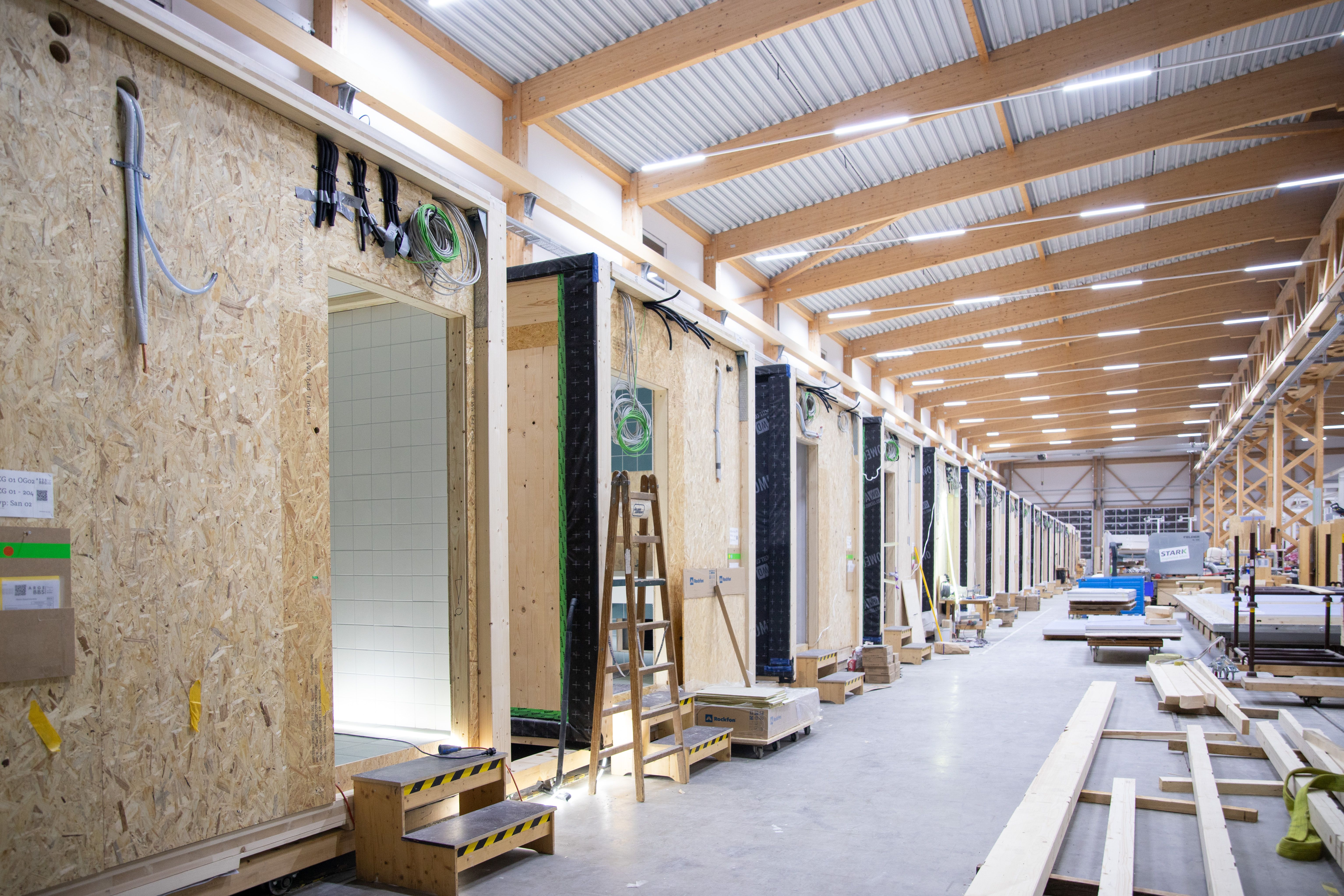 Reihe vorgefertigter Sanitärmodule in der Produktionshalle mit Holztragwerk