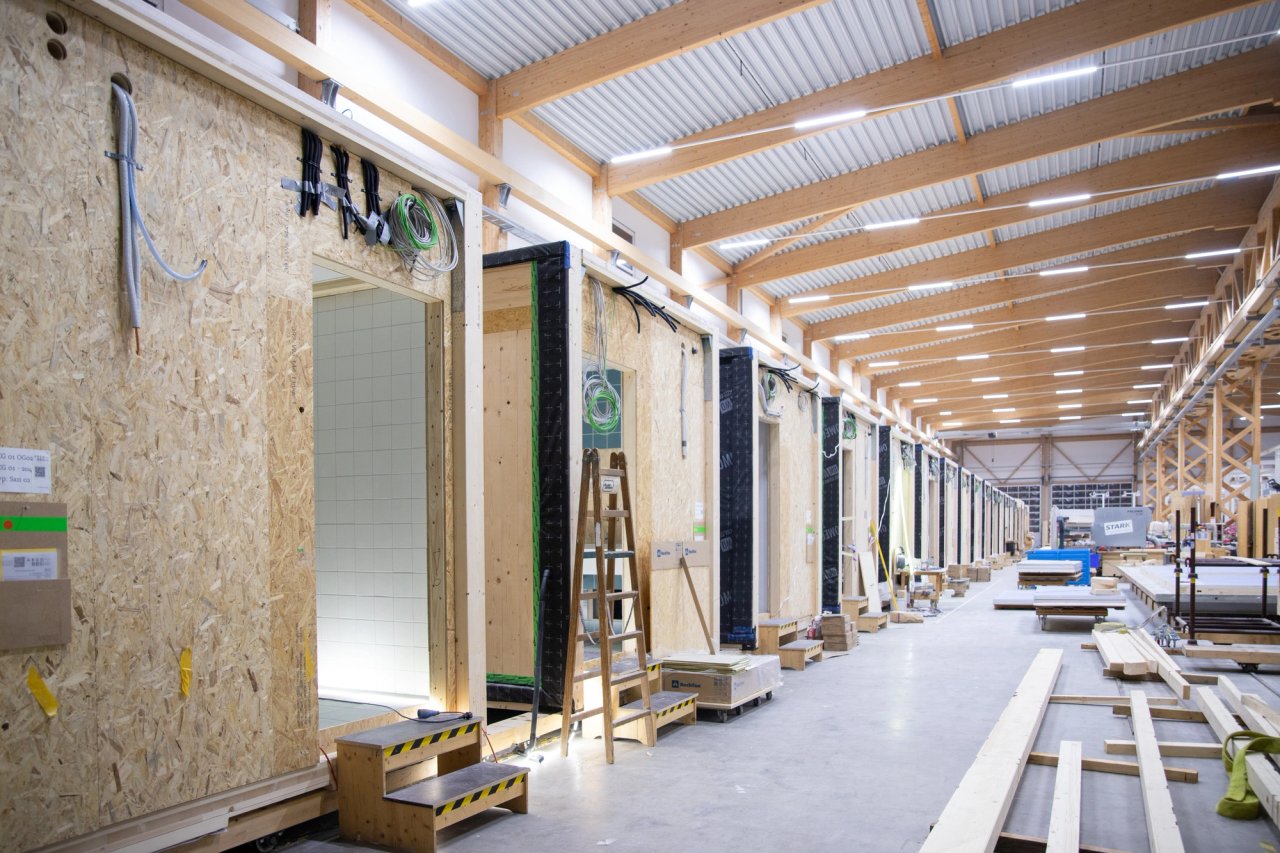 Reihe vorgefertigter Sanitärmodule in der Produktionshalle mit Holztragwerk