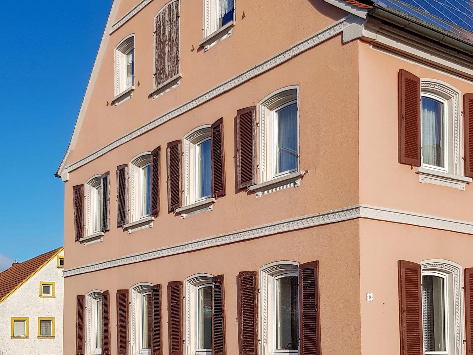 Unsanierte Fassade in Altrosa mit braunen Klappläden