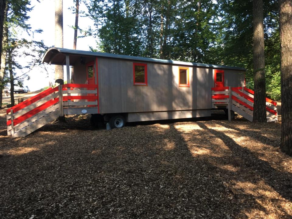 Grauer Waldkindergartenwagen mit roten Treppengeländern zwischen Kiefern auf Waldboden