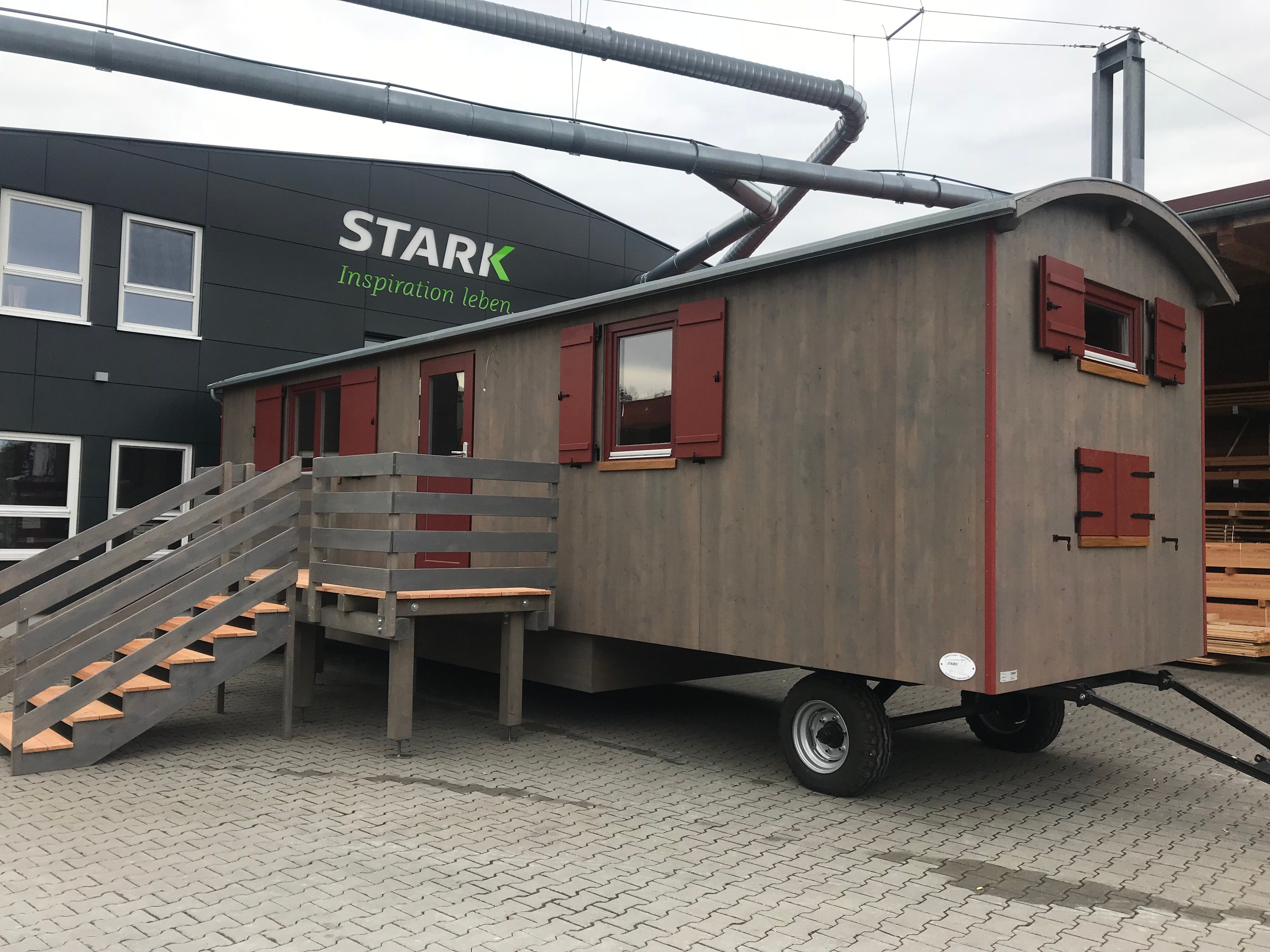 Graubrauner Waldkindergartenwagen mit roten Fensterläden, Podest und Treppe vor dem Firmengebäude der Zimmerei