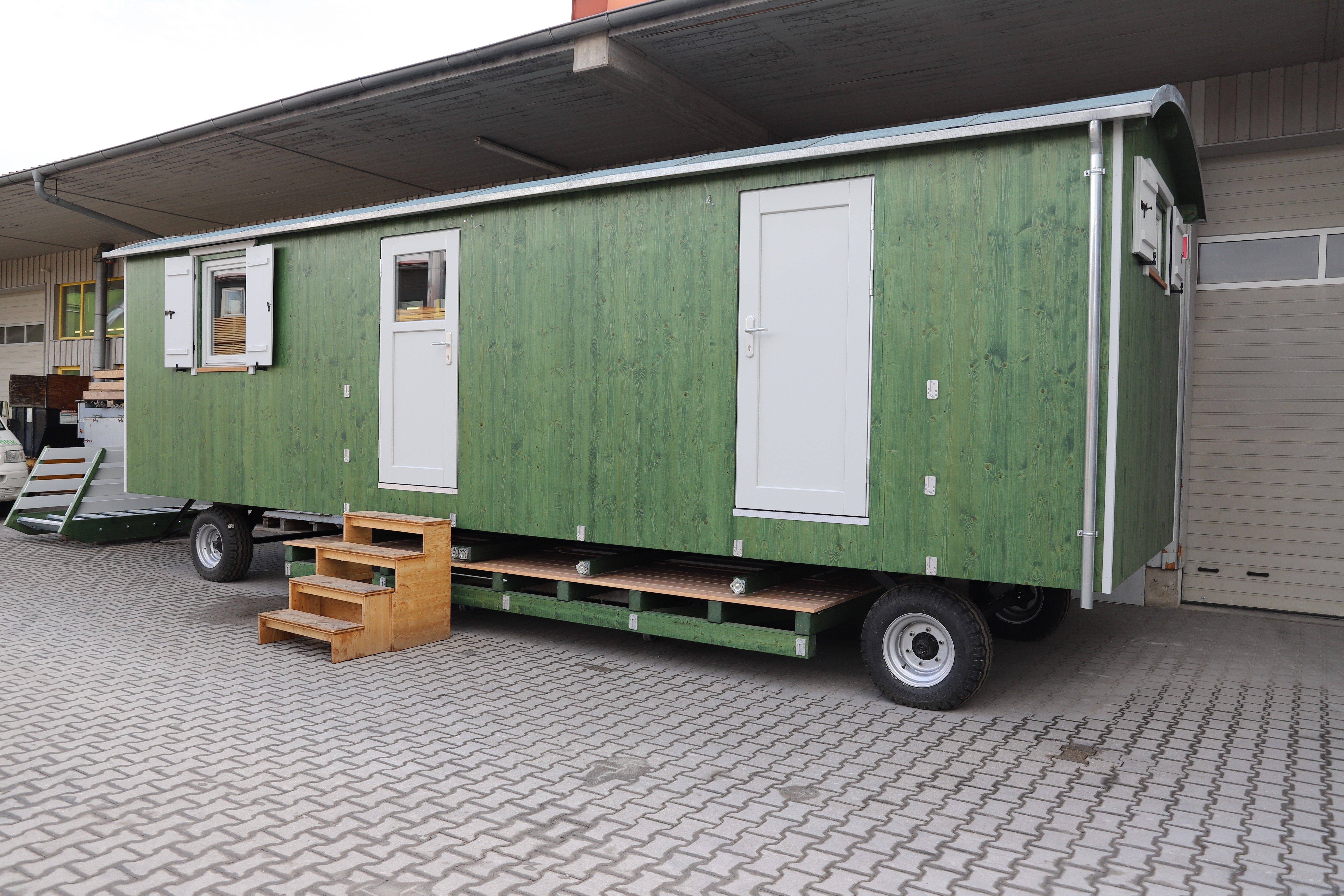Langer grüner Waldkindergartenwagen mit zwei weißen Türen und Fensterläden, von der Seite gesehen