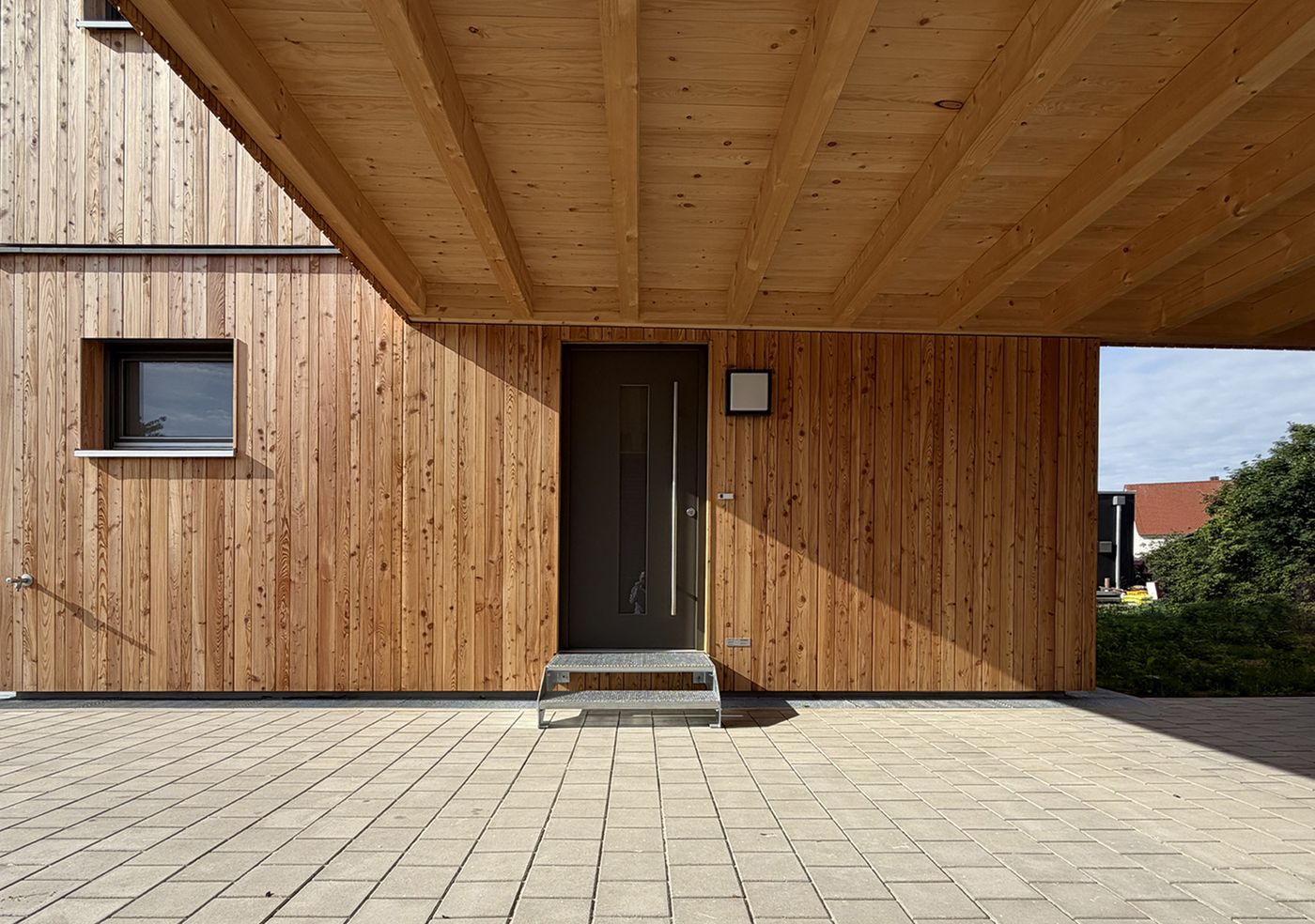 Holzfassade, geschützter Eingang und Carport gehören zur Architektur des Hauses.