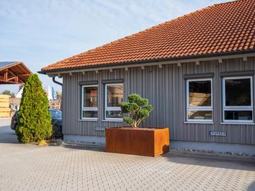 Ecke des Ausstellungsgebäudes mit Ziegeldach, grauer Holzfassade und Cortenstahl-Pflanzkübel