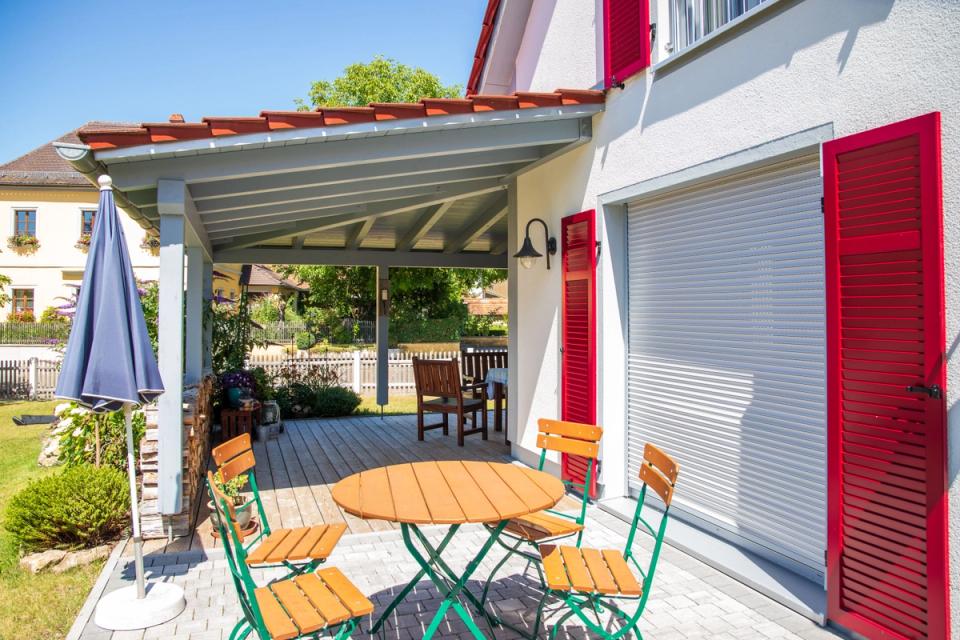 Terrasse mit Bistrotisch, roten Fensterläden und Rollladen-Garage