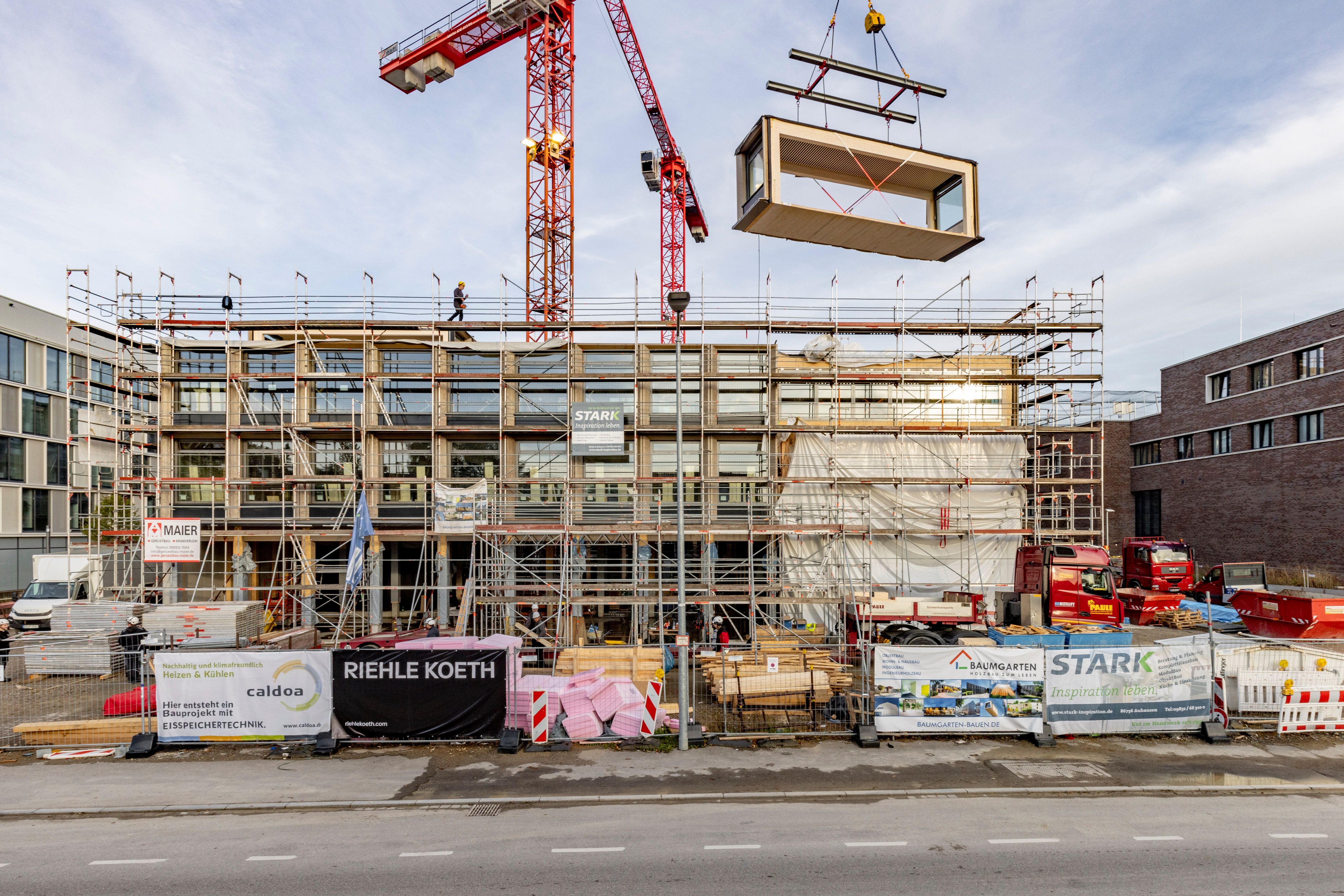 Holzmodul schwebt am Abend über dem eingerüsteten Neubau