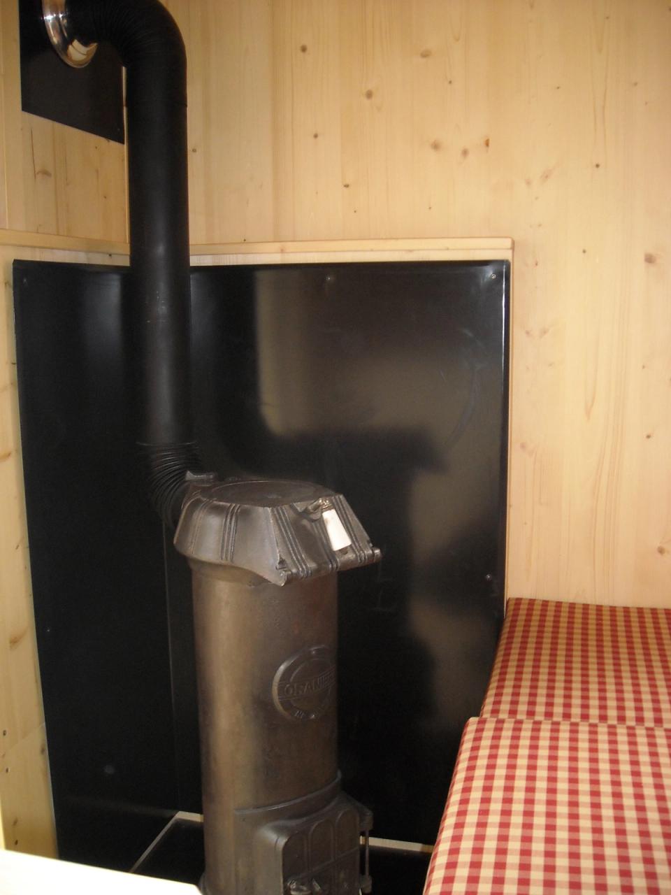 Kleiner Holzofen mit Ofenrohr vor einer schwarzen Schutzwand im Jagdwagen