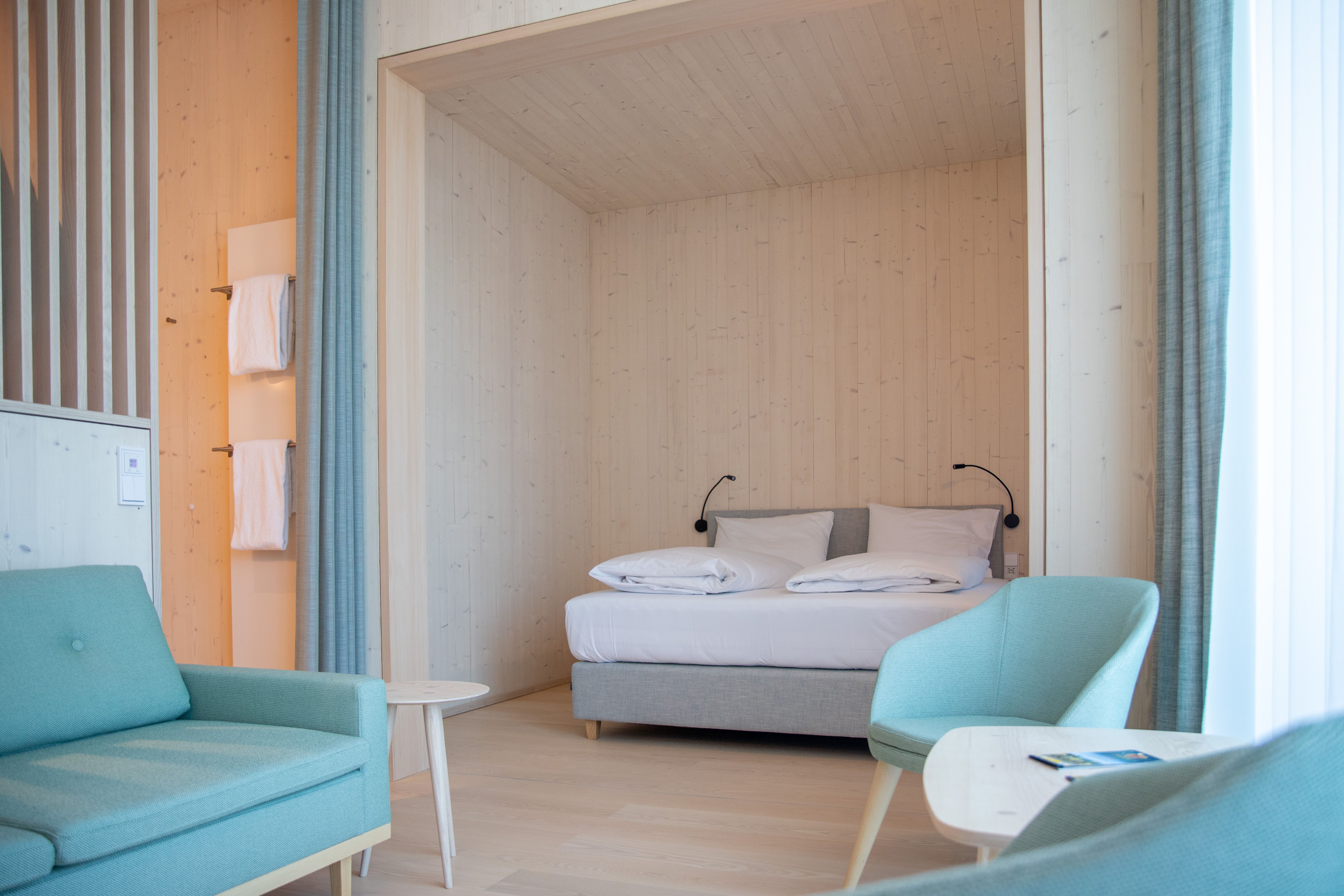 Hotelzimmer mit Schlafnische aus hellem Holz und türkisen Sesseln